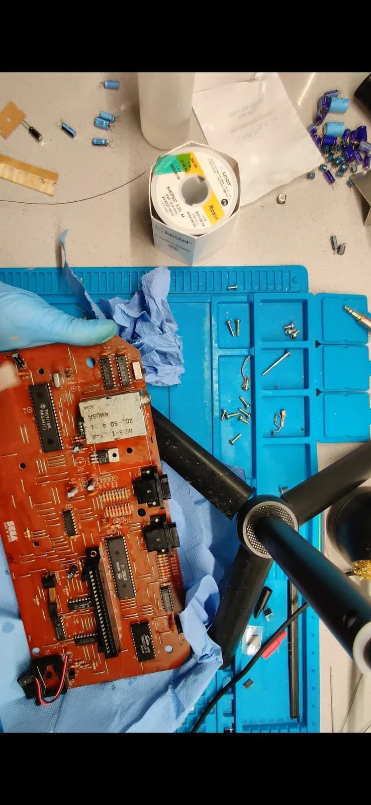 Sega SG-1000 II red main board, already recapped, on a blue work mat with a solder spool, the old removed capacitors, loose screws, and an empty Console5 capacitor-kit bag.