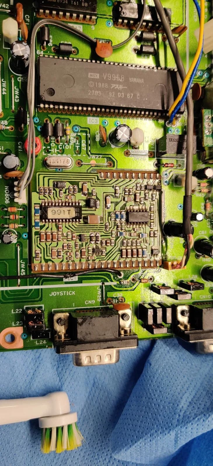 Sony HB-F1XV mainboard with HIC-1 audio board undergoing SMD capacitor replacement using MLCC caps; cleaning brush visible.
