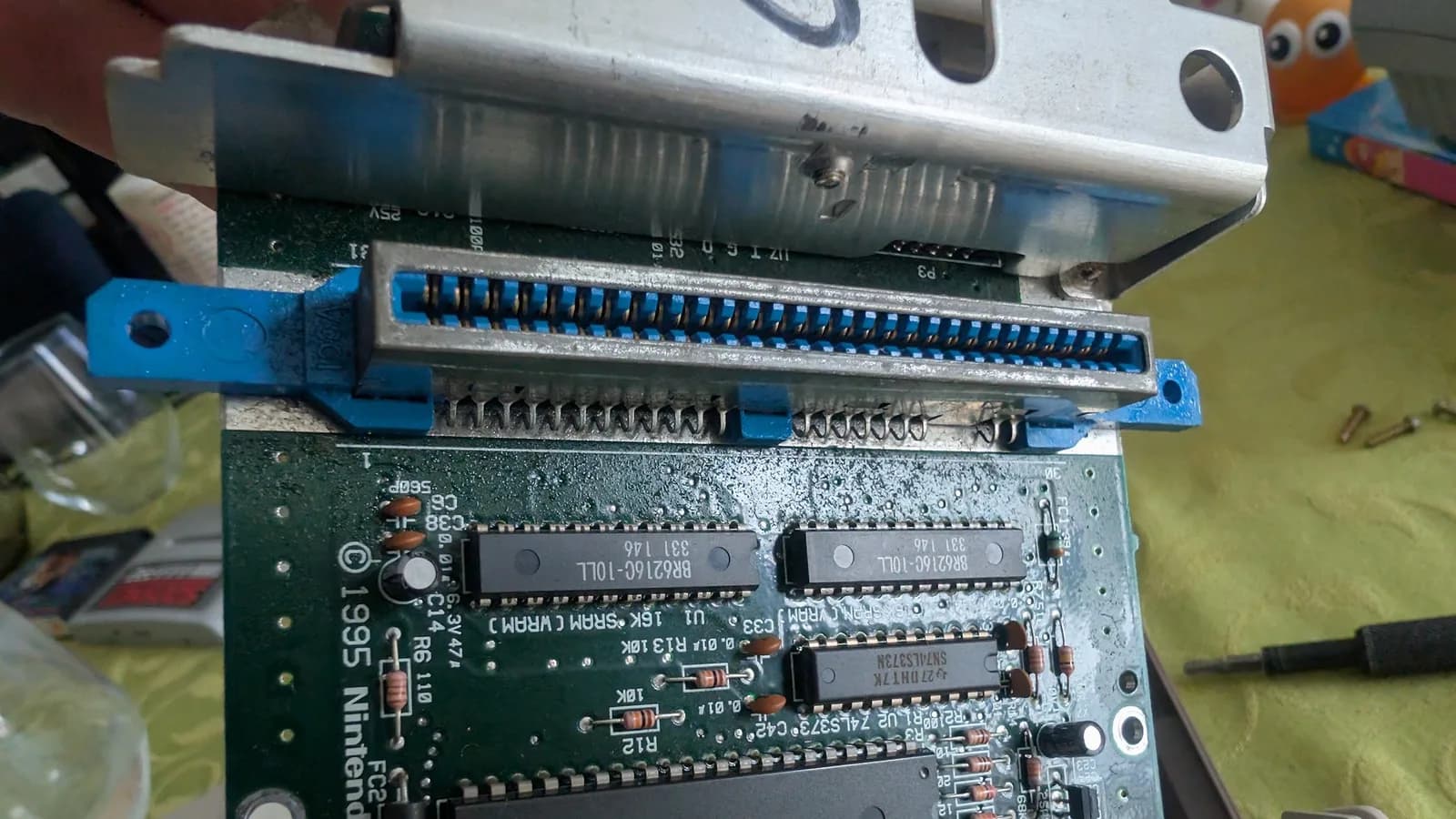 Close-up of the AV Famicom motherboard focused on the cartridge-slot edge connector (its blue plastic body) and nearby IC chips, with a film of dust and residue across the board.