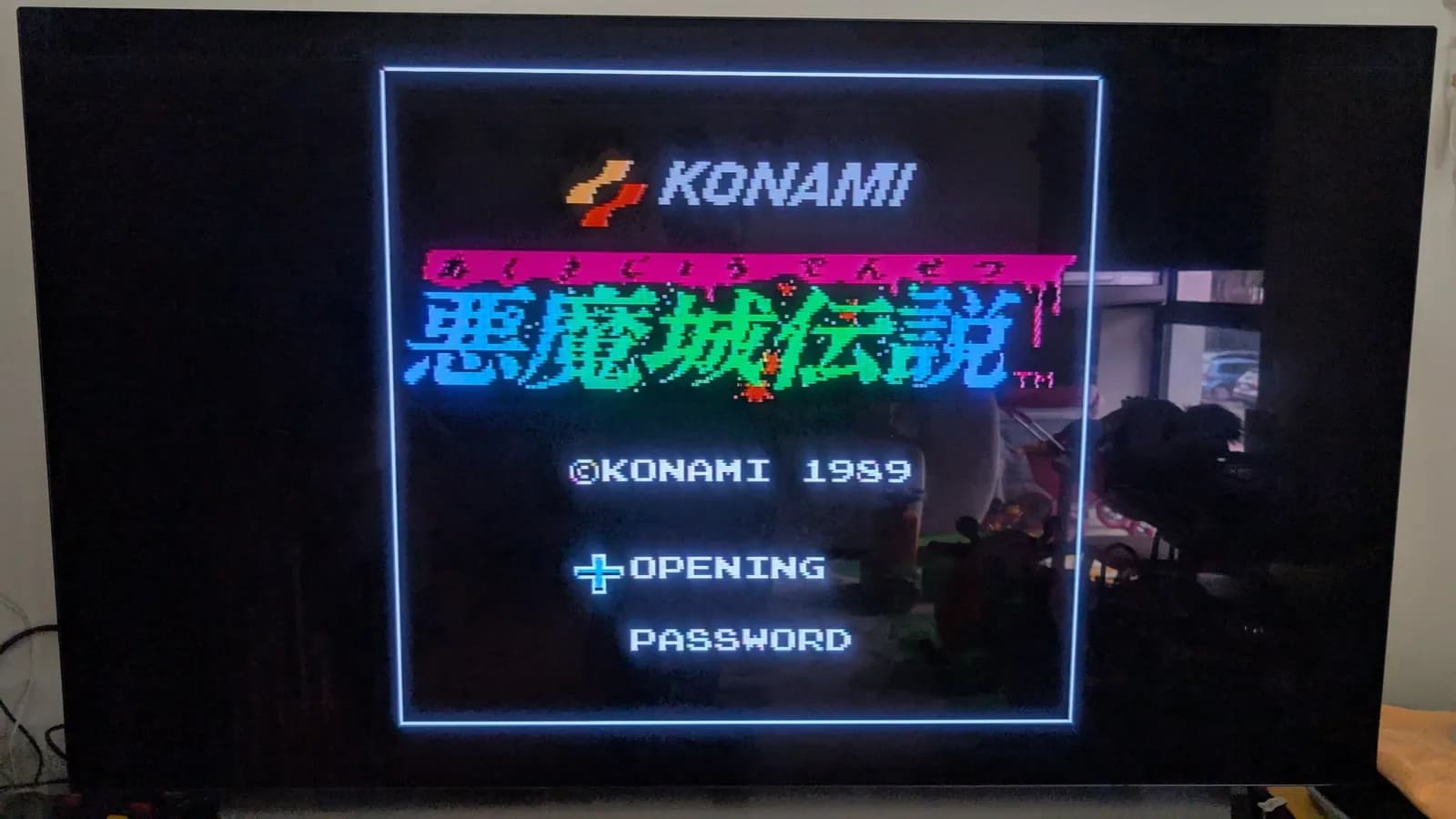 Konami Castlevania III (Akumajo Densetsu) title screen on an LG C1 OLED TV, output from the AV Famicom after its cartridge slot was cleaned. Shows the KONAMI 1989 logo and the OPENING and PASSWORD menu.