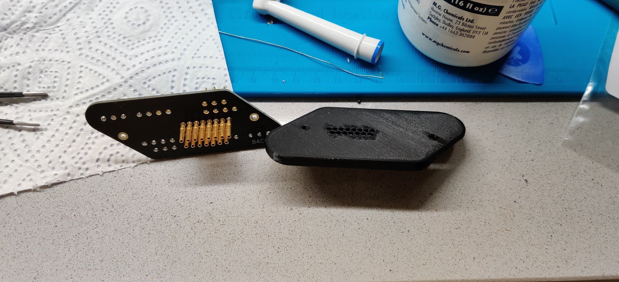 Twin Famicom wireless controller connector with gold-plated pins and black plastic housing, alongside repair supplies on workbench.