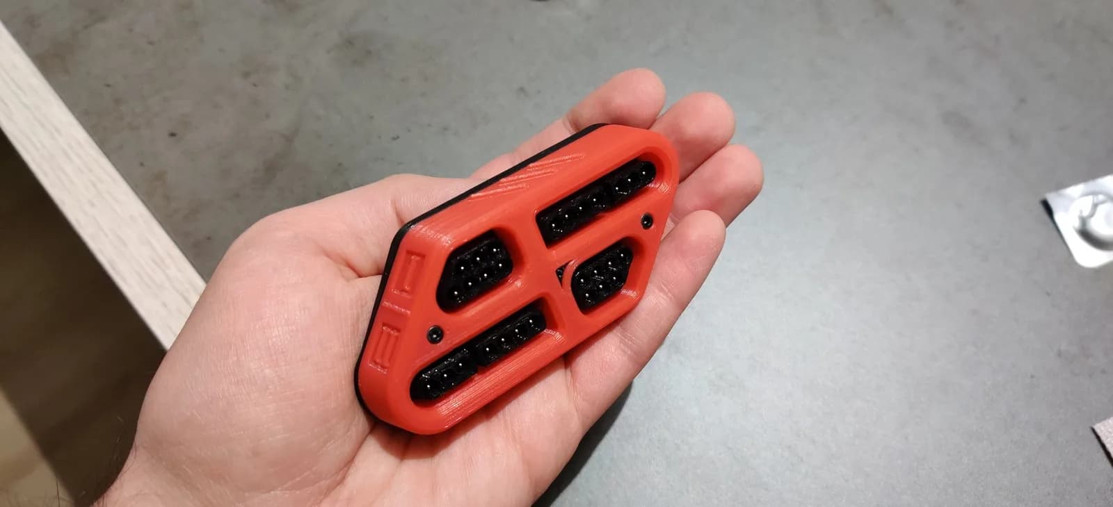 The assembled red and black 3D-printed TwinDiamond accessory held in hand, the PCB fully enclosed between the printed parts, with the controller-port openings visible on the shell.