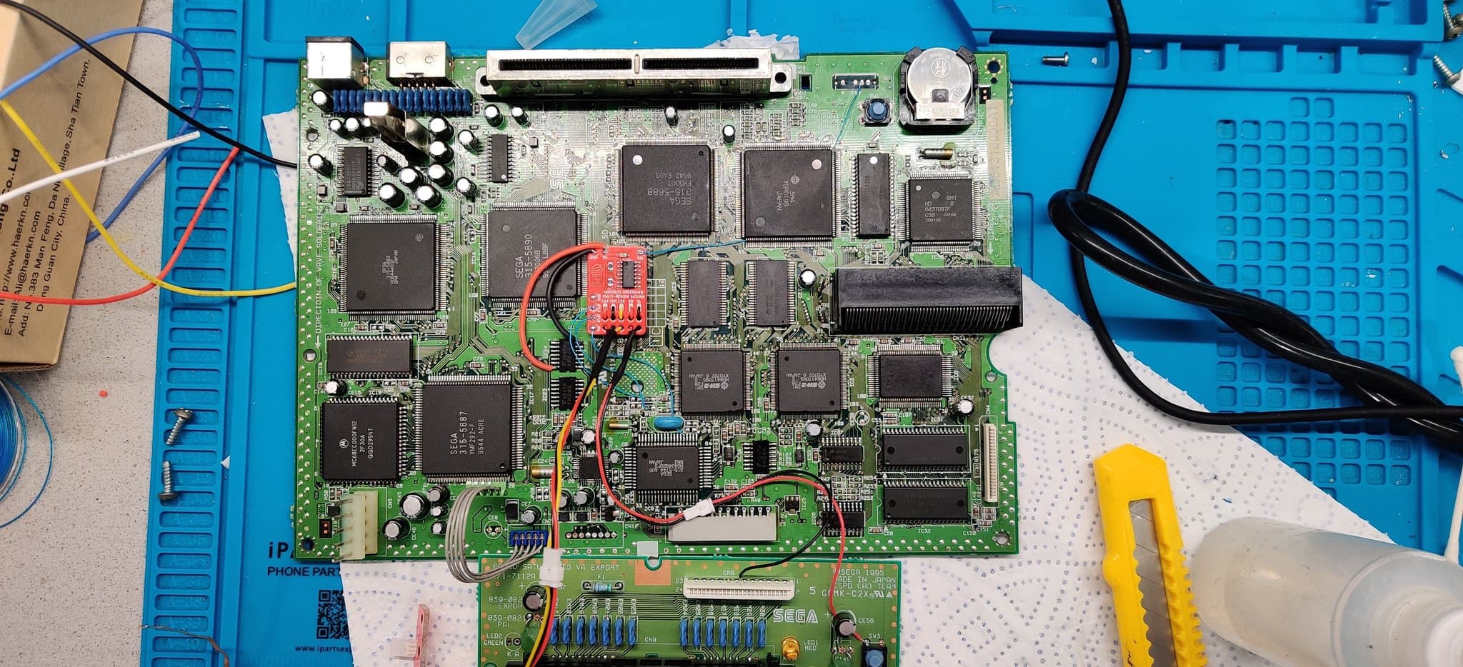 Sega Saturn mainboard with 50/60Hz mod installed; red modchip visible center-board with soldered connections to nearby IC chips.