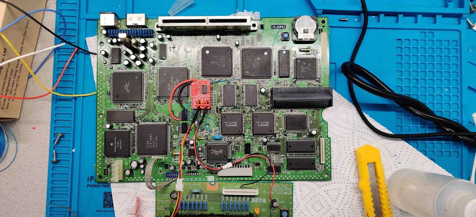 Sega Saturn mainboard with 50/60Hz mod installed; red modchip visible center-board with soldered connections to nearby IC chips.