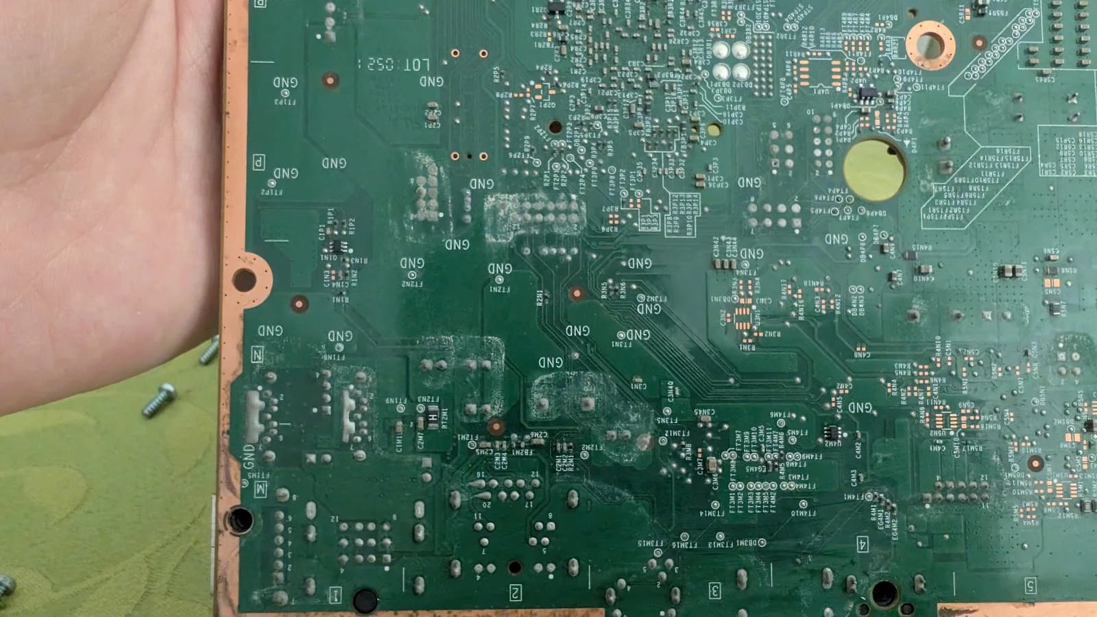 Xbox 360 E motherboard (solder side) with whitish liquid-spill residue and oxidation across the board and components; the console still worked, so this was preventative cleanup.