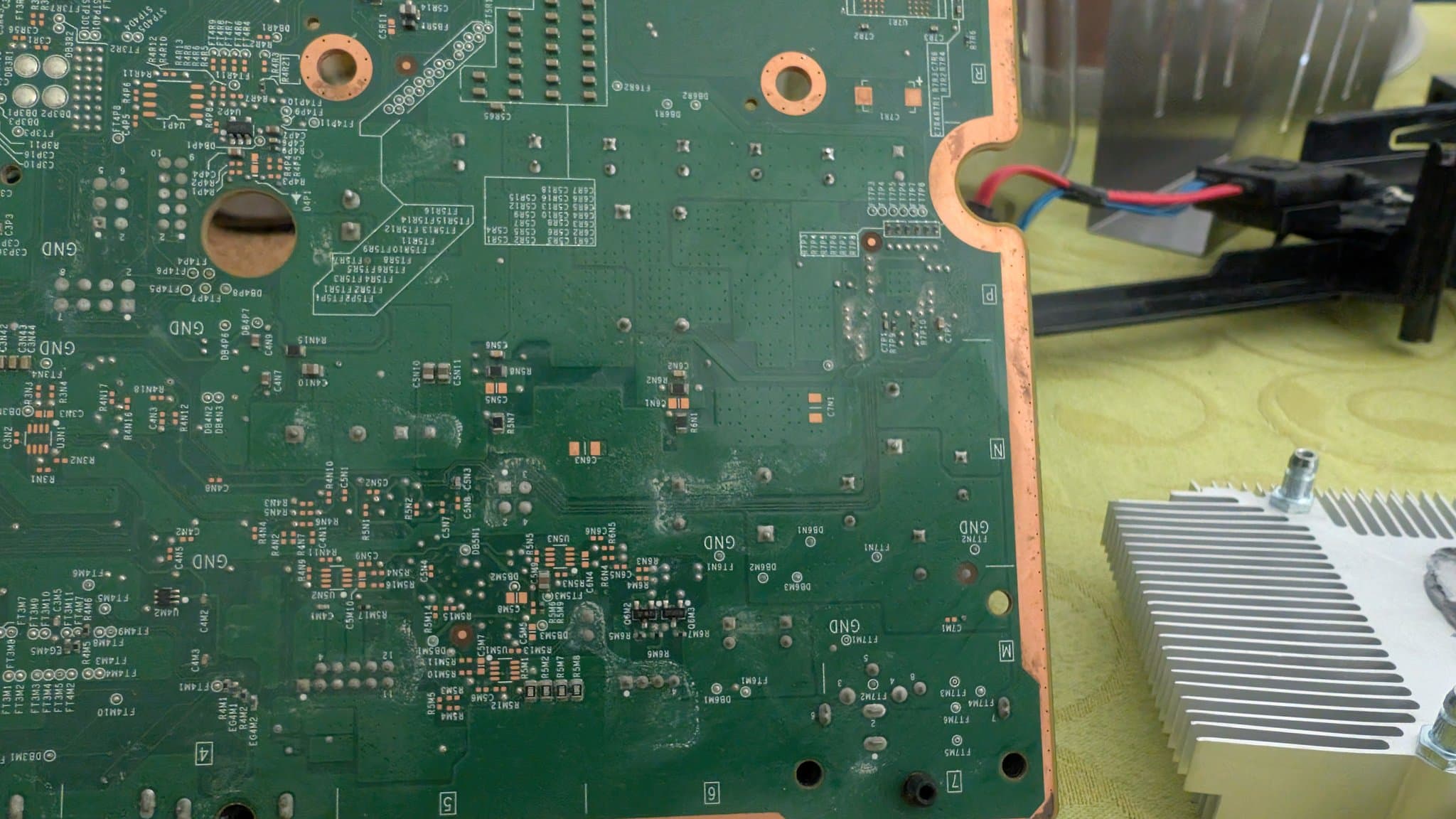 Xbox 360 E motherboard showing liquid damage residue, with heatsink removal in progress and power supply recap work visible.