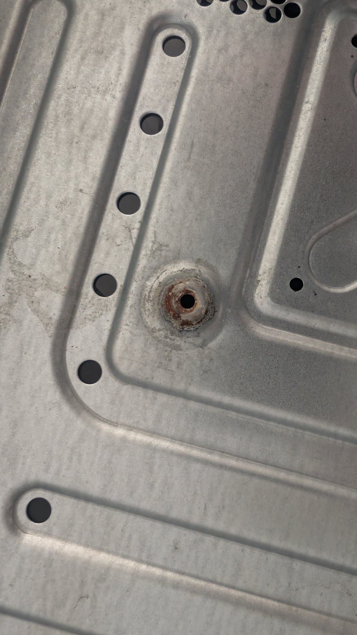 Rusted metal shield on Xbox 360 E motherboard with evaporust treatment applied; corrosion visible around fastener hole.