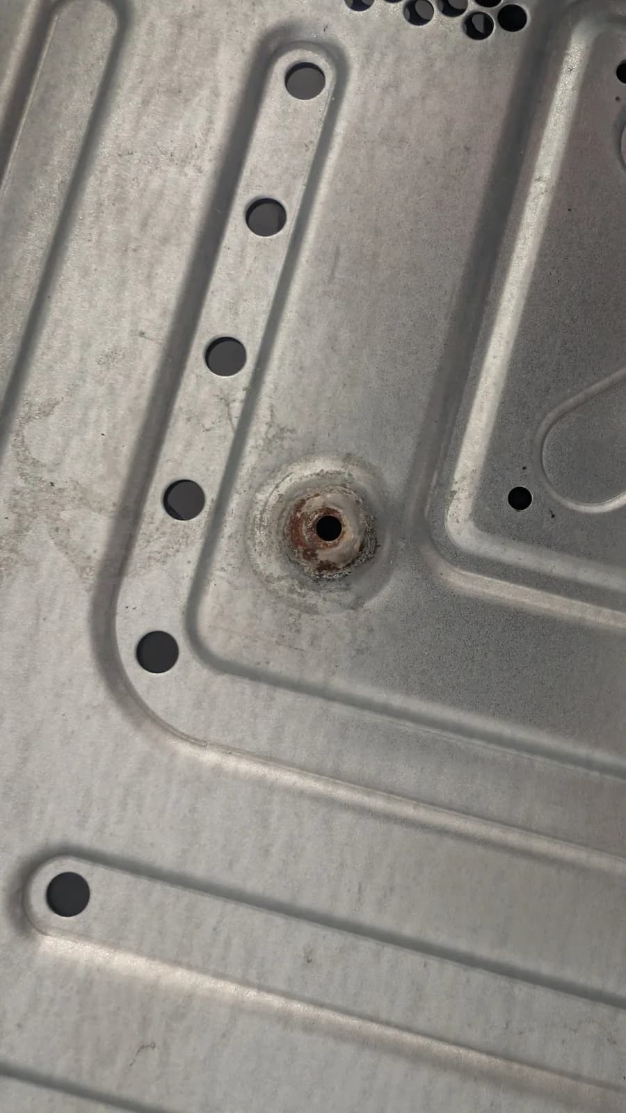 Rusted metal RF shield from the Xbox 360 E, with orange corrosion around a central fastener hole and whitish staining on the galvanized surface.