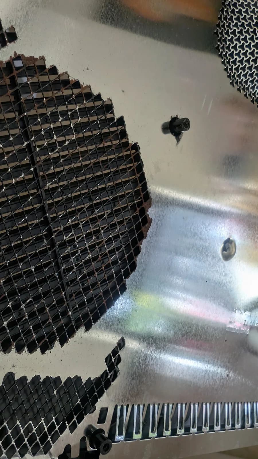 Close-up of a rusty metal RF shield from the Xbox 360 E, with orange corrosion around the mesh ventilation grilles and a mounting post.
