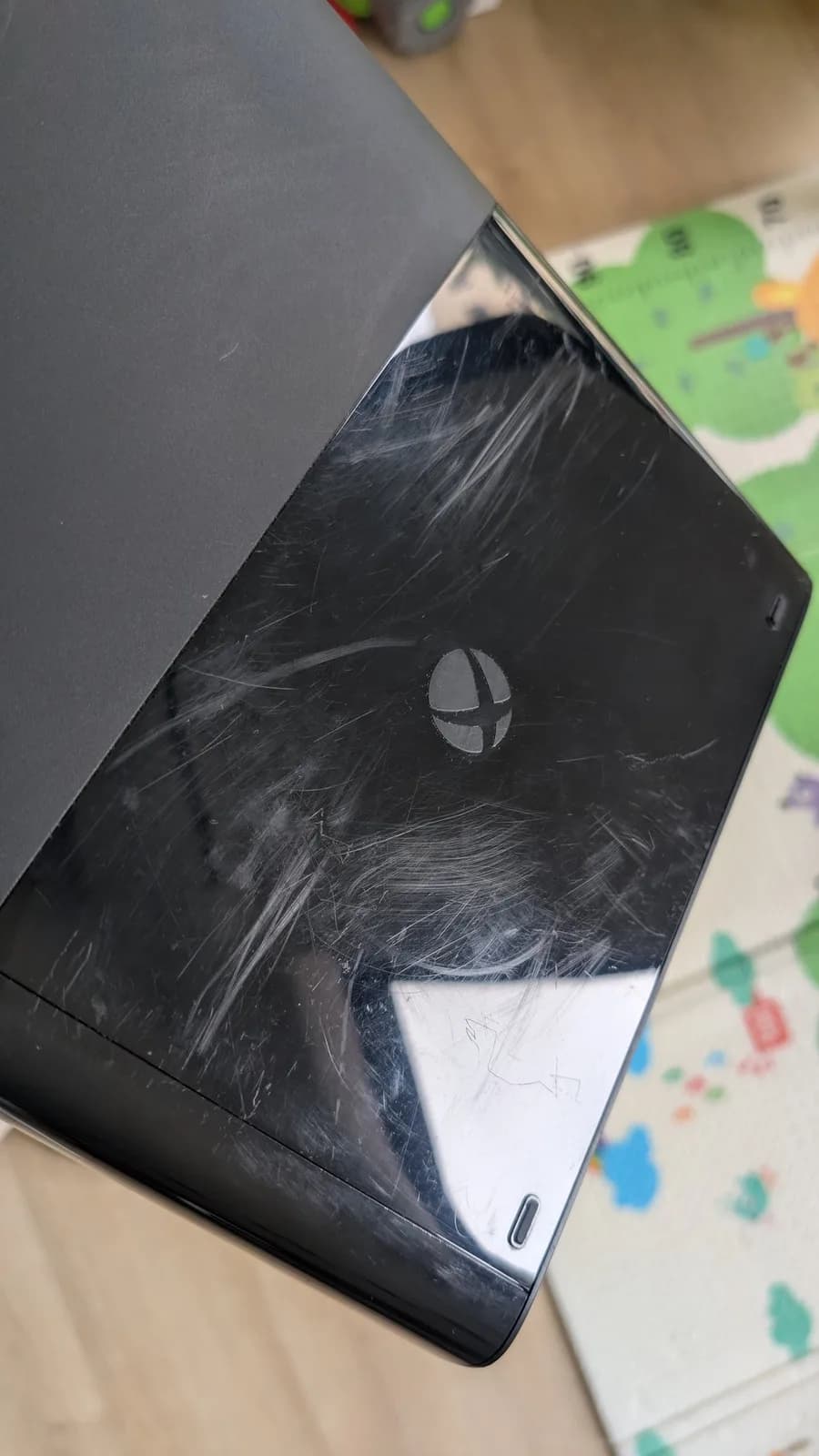 Xbox 360 E shell showing deep scratches and scuff marks on black casing during cleaning restoration.