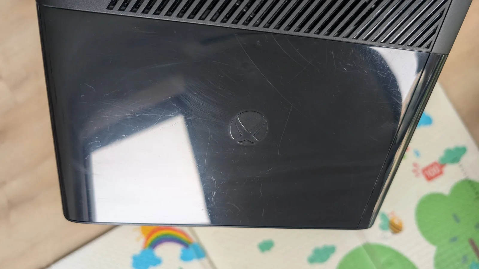 Xbox 360 E black plastic shell after polishing, with far fewer scratches and a glossy finish restored, only a few scuffs remaining.