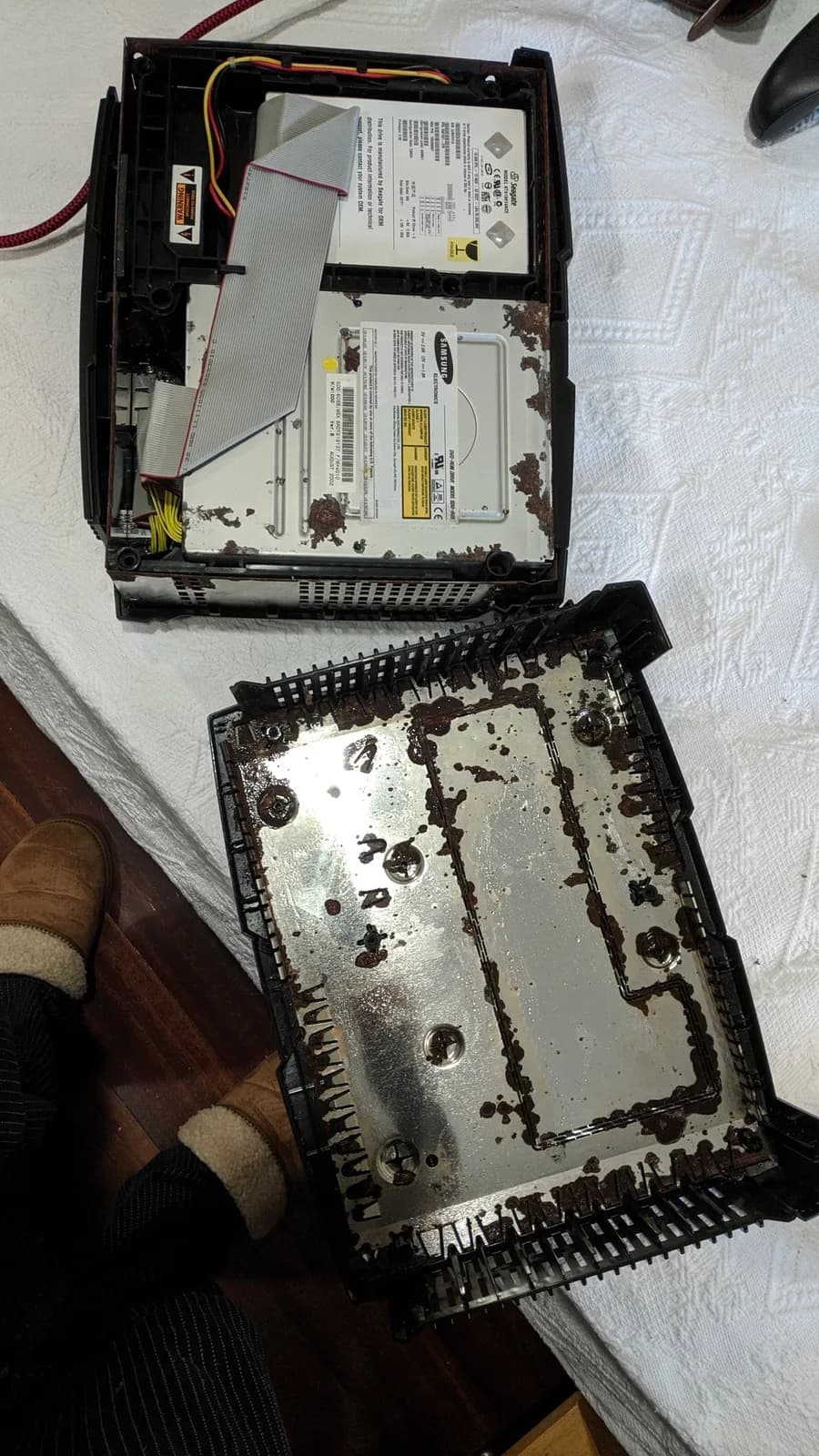 Disassembled OG Xbox showing heavily corroded metal chassis and optical drive assembly with visible rust, capacitors, and ribbon cables during refurbishment.