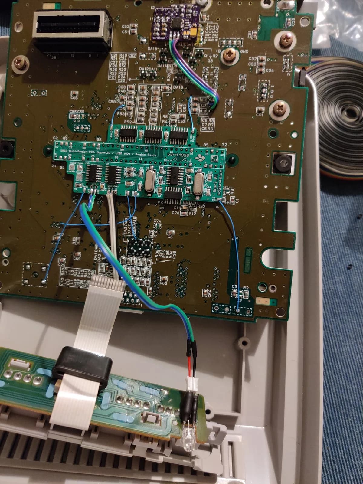 SNES 1-chip motherboard with lifted CPU pins, region switch mod wiring, and LED installation in progress during modification work.