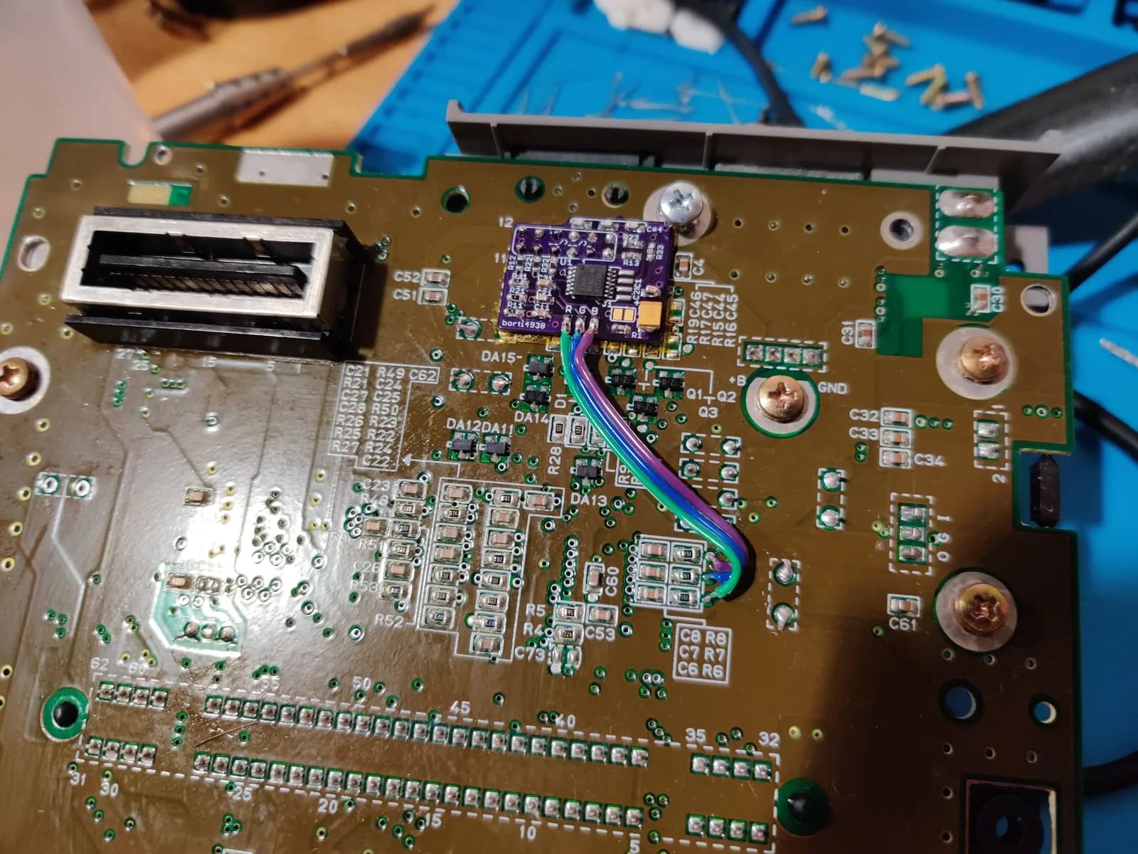 Close-up of SNES motherboard with purple 1-chip mod board installed, showing transformer, capacitors, and soldered ribbon cable connections.