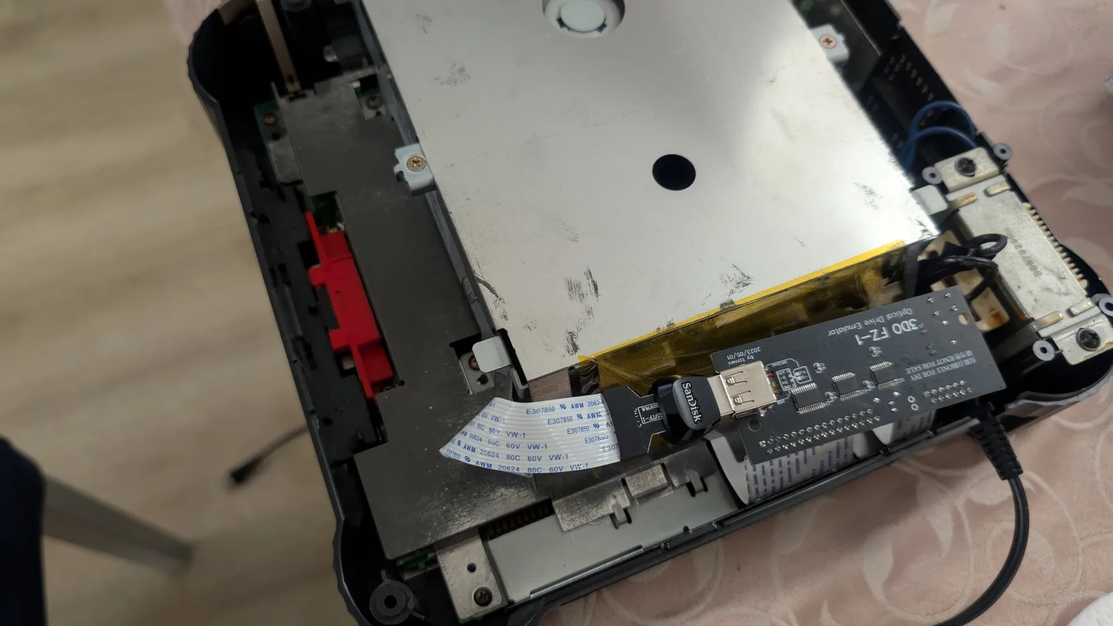 An opened Panasonic FZ-1 3DO on a patterned tablecloth, its metal drive shielding exposed; the black 3DO FZ-1 ODE board connected by a ribbon cable with a SanDisk USB flash drive plugged into it.