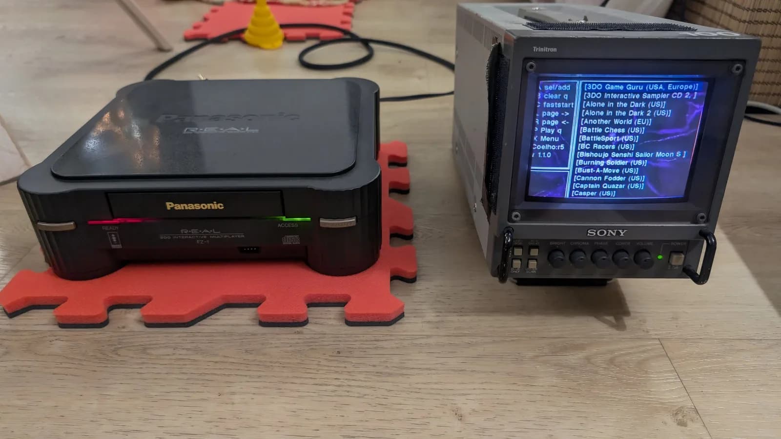 The finished Panasonic FZ-1 3DO (red READY and green ACCESS LEDs lit) on a red foam mat, next to a Sony PVM-6041Q broadcast monitor showing the ODE's 3DO game-selection menu (Alone in the Dark, Cannon Fodder, Bust-A-Move and more).