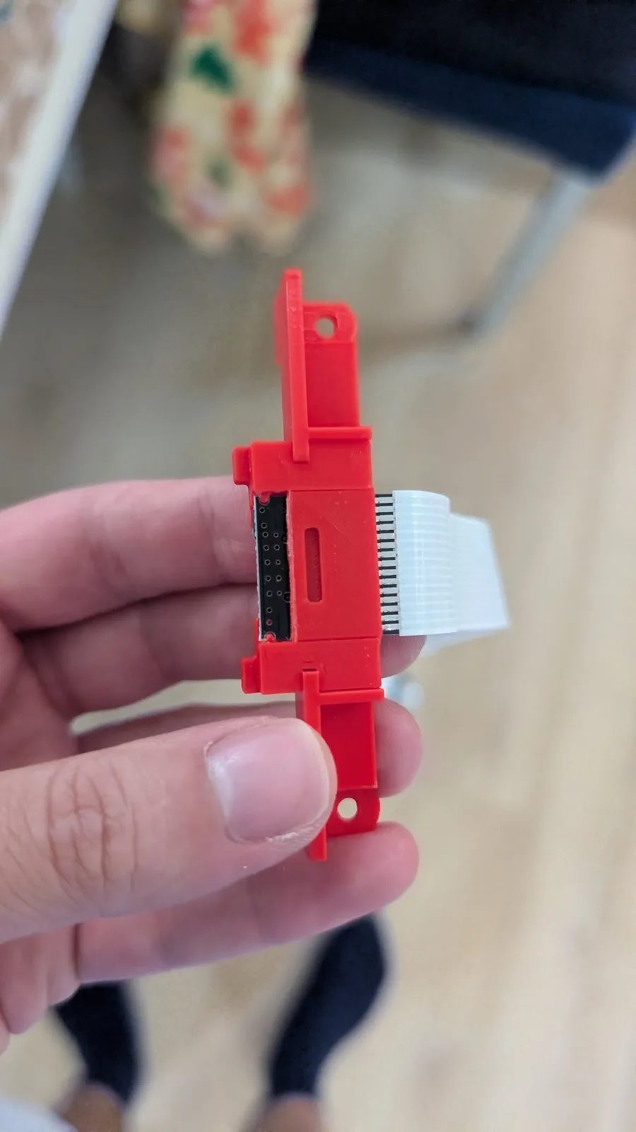 Red 3D-printed SD card extender adapter for 3DO ODE, showing connector pins and white ribbon cable, held in hand during installation.