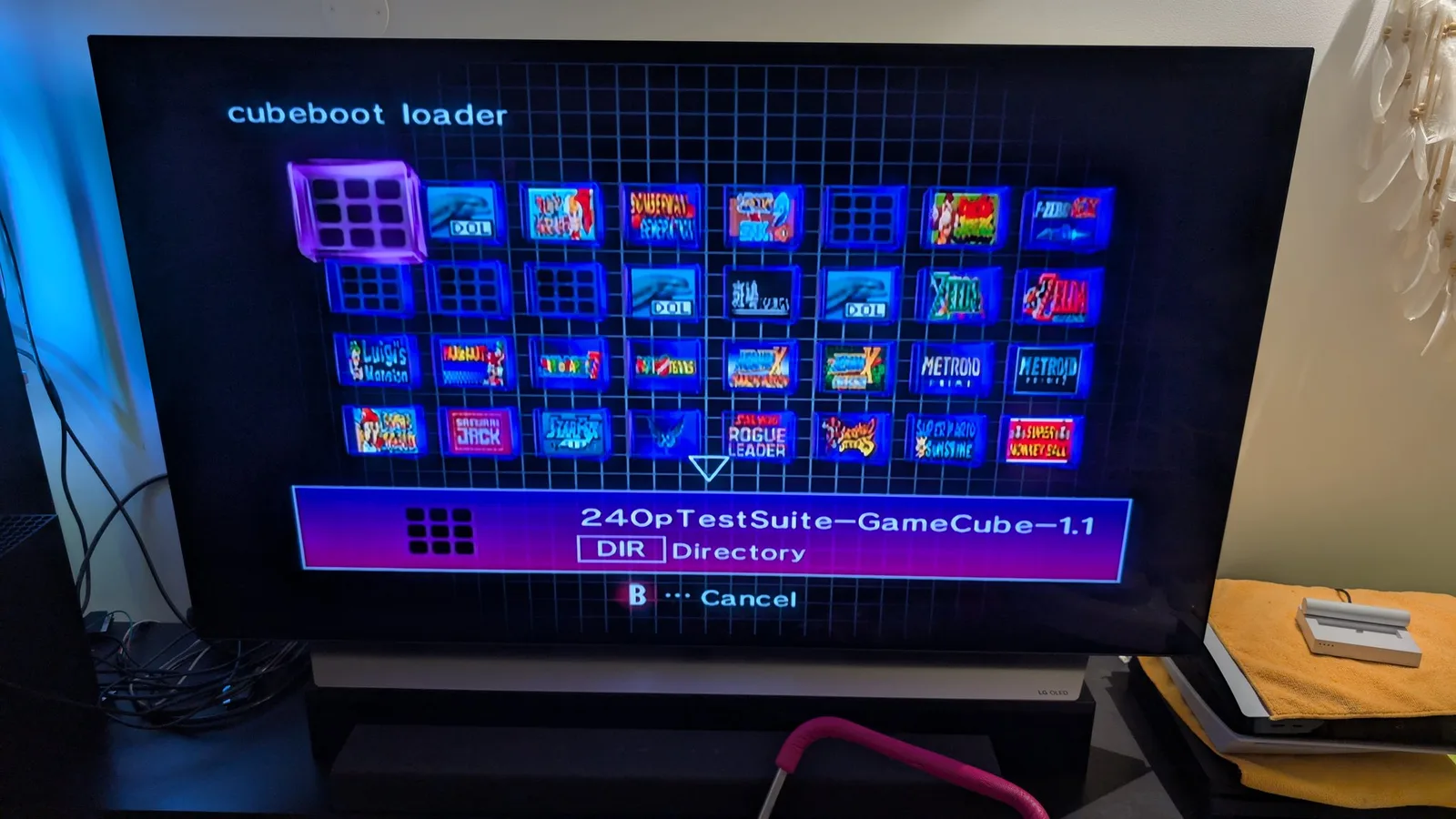 The FlippyDrive's cubeboot loader menu on an LG OLED TV, a grid of GameCube cover thumbnails with the '240pTestSuite-GameCube-1.1' directory selected at the bottom.