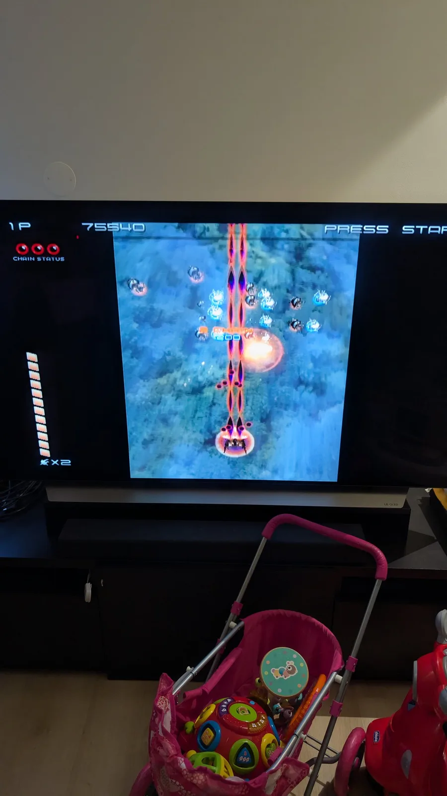 Ikaruga running on an LG OLED TV (its CHAIN STATUS meter, score 75540 and ship count on screen), a pink toy pram in front, testing the spice orange GameCube after the FlippyDrive install.