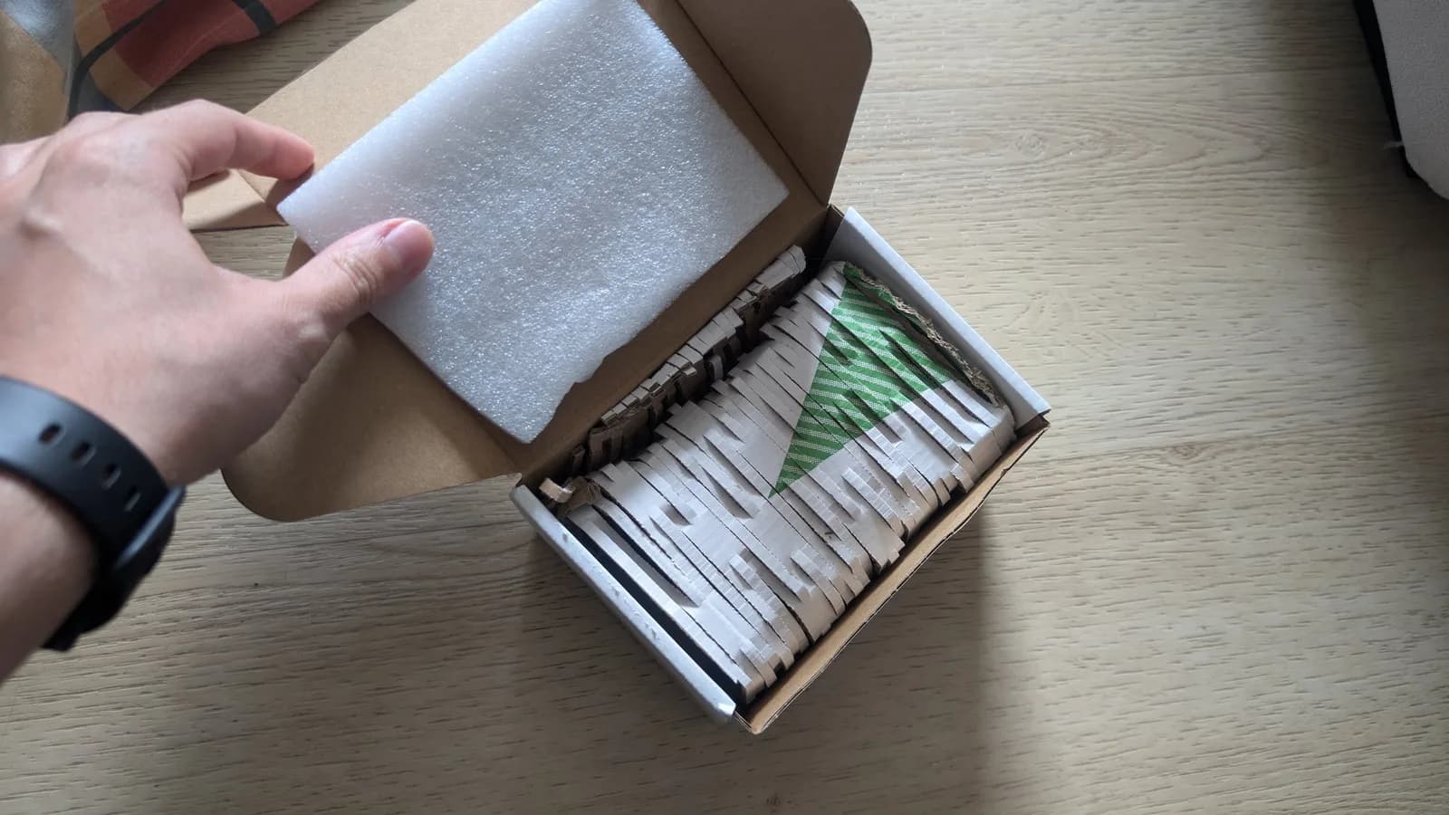 Hand opening box containing new aftermarket Nomad battery pack with foam padding and green branded label visible inside.