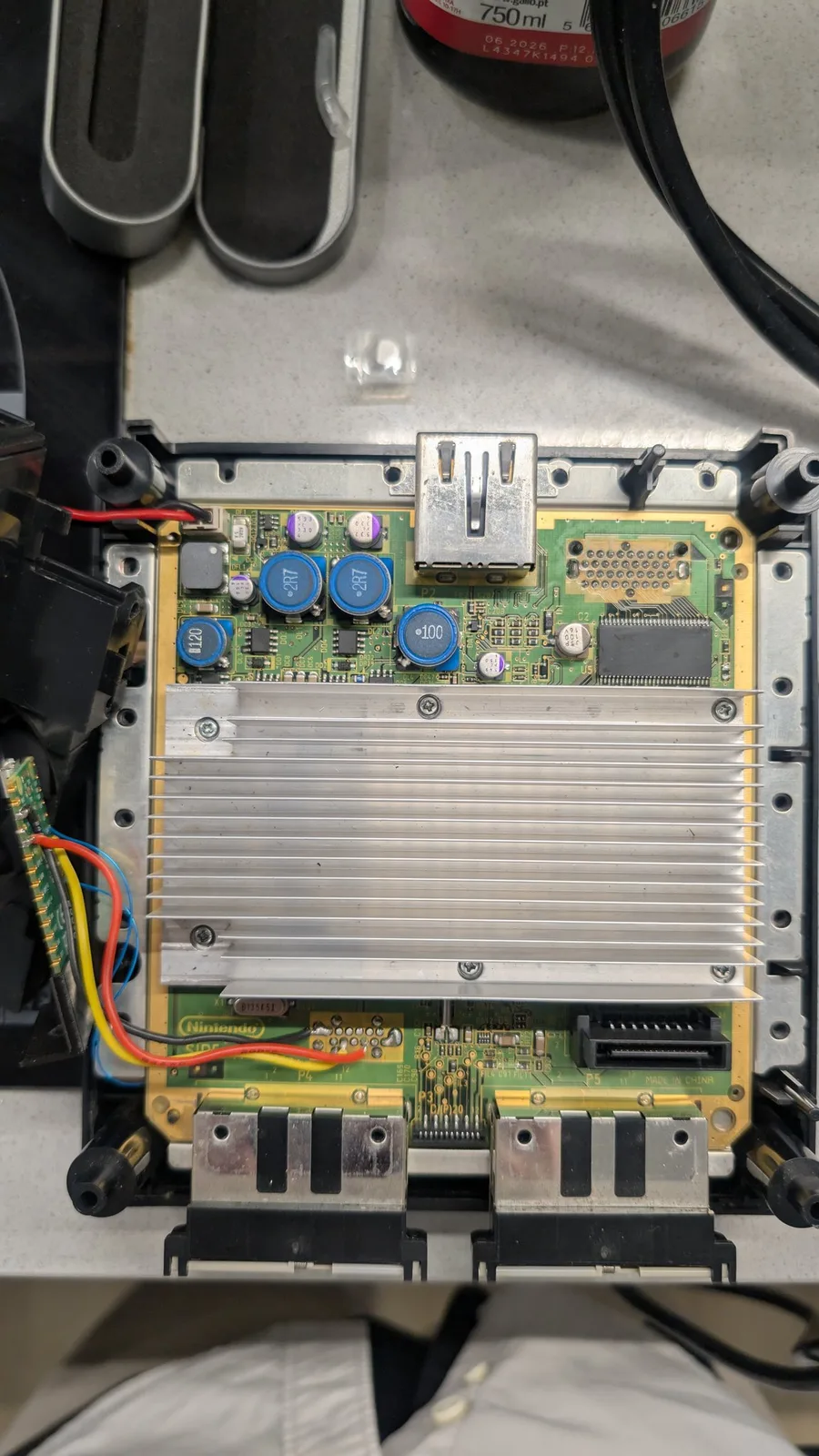 The PAL DOL-101 GameCube mainboard with the PicoBoot mod installed, its blue inductors and aluminium heatsink visible, and its five grey metal-can SMD capacitors: four purple-striped (polymer) and one black-striped (likely electrolytic, and the one replaced in this minimal recap).