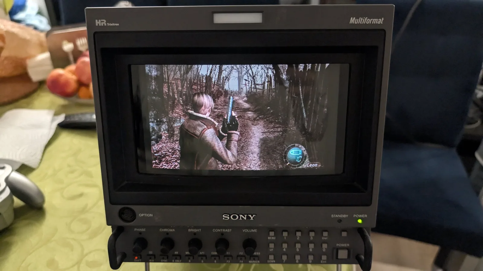 A Sony BVM-D9H5J monitor displaying Resident Evil 4 gameplay (Leon aiming a handgun in a forest), run from the spice orange GameCube via its PicoBoot; the console is off-frame.