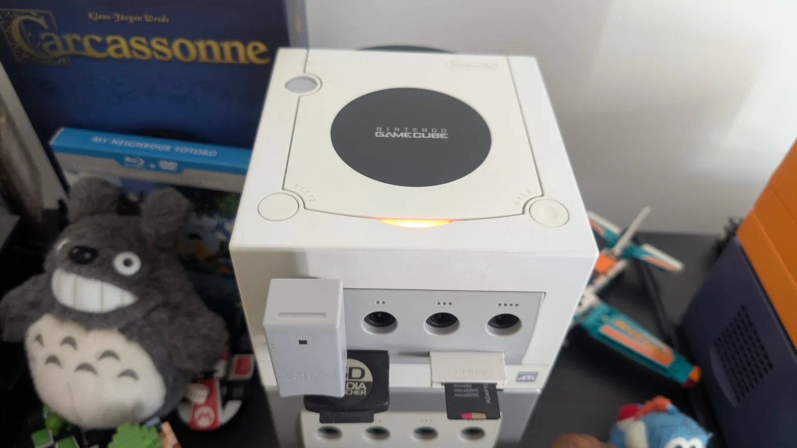 Pearl white Nintendo GameCube with DOL-001 board in DOL-101 shell, optical drive visible, surrounded by gaming collectibles during restoration testing.