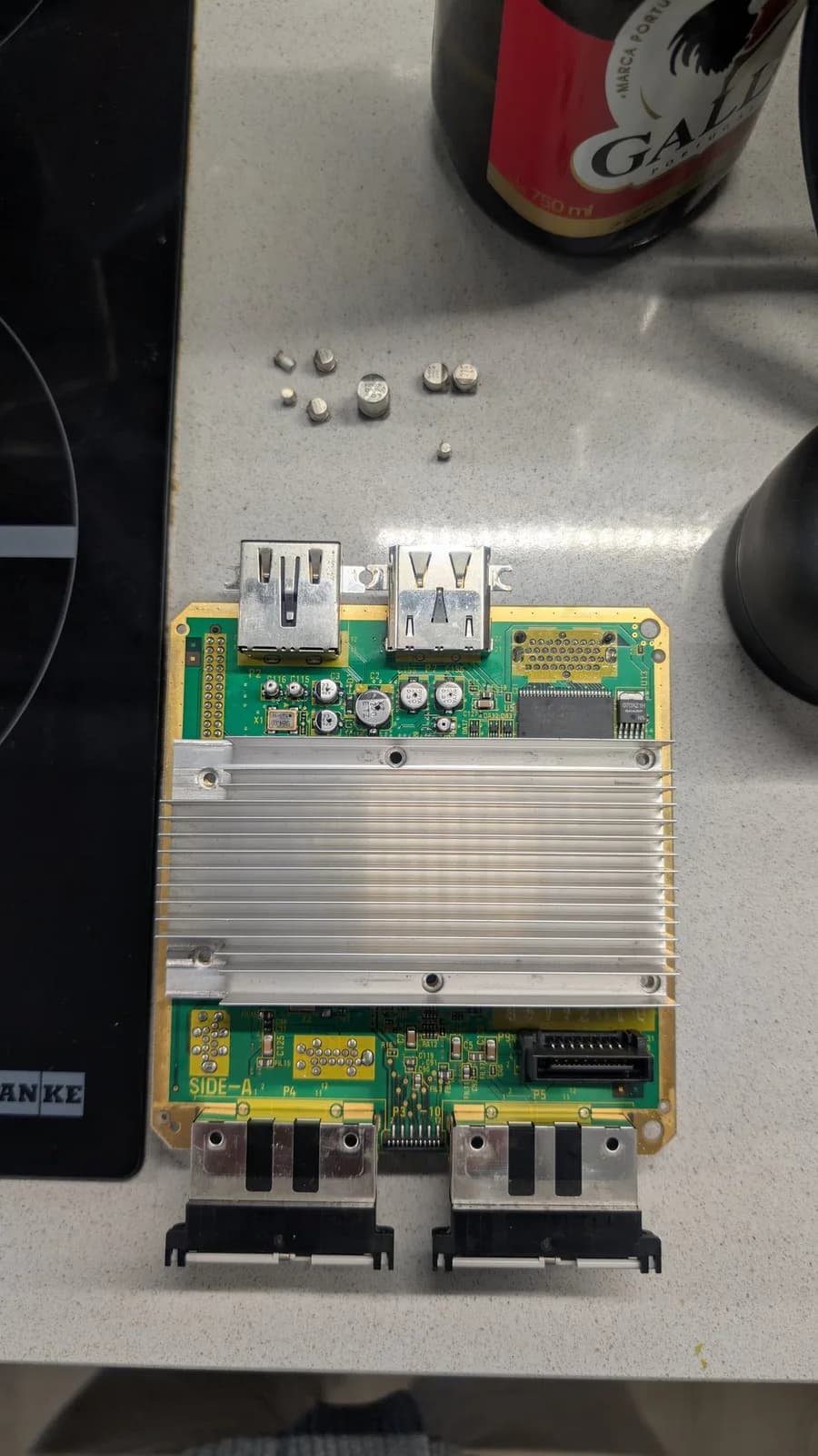 Disassembled GameCube mainboard with capacitors removed, aluminum heatsink, and replacement caps laid out on work surface.