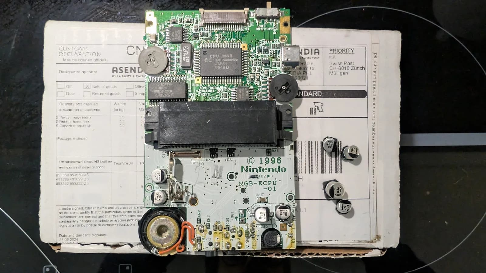 Game Boy Pocket after the recap: the board in its shell with the fresh capacitors installed and the old ones removed and set on the Console5 box to the right. The two brightness and volume trimmer wheels, the speaker and the MGB-ECPU-01 power section are visible.