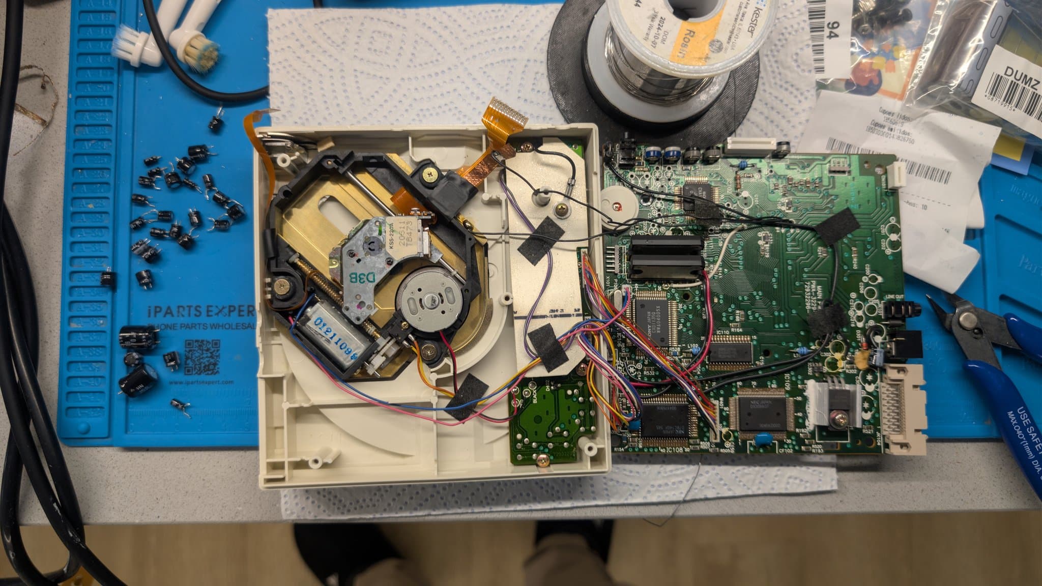 Disassembled PC Engine CD-ROM2 during the recap: the green mainboard on the right with all its electrolytic capacitors removed, and the old removed caps laid out on the blue mat.