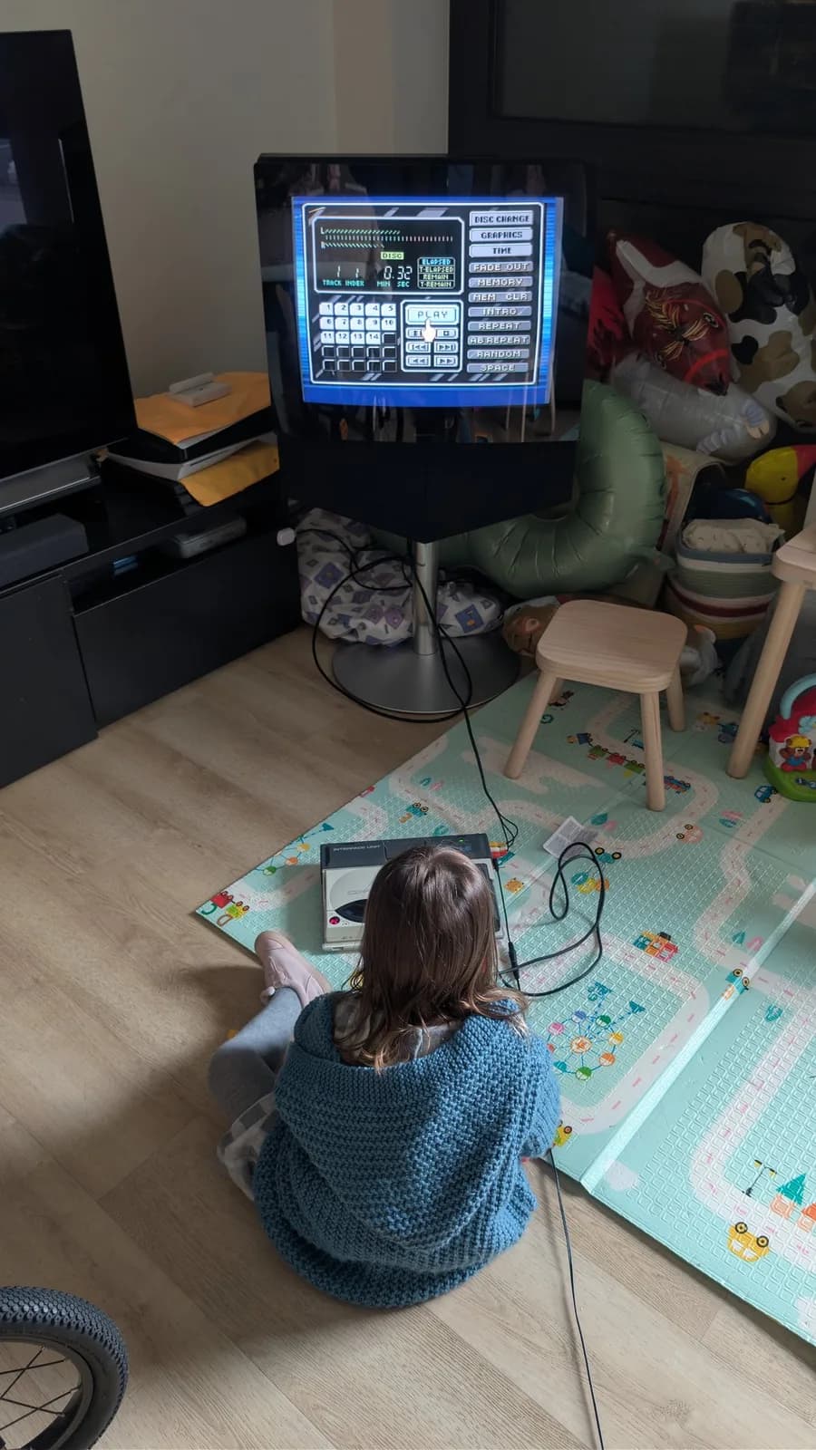Child sitting on play mat facing restored NEC PC Engine CD-ROM2 displaying menu screen on CRT monitor, playing Castle in the Sky OST.