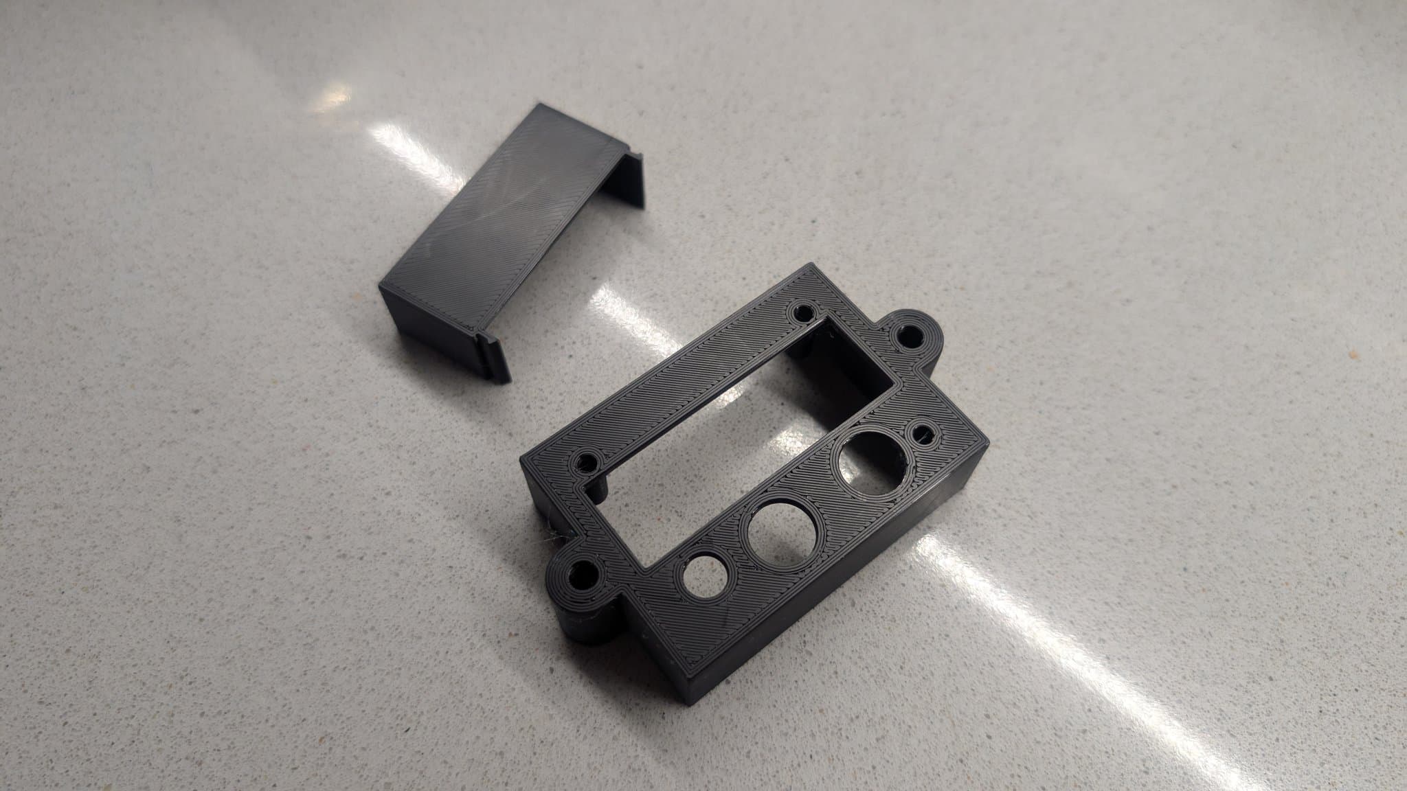 3D-printed black plastic shell components for PVM-14L1 RGB mod, showing rectangular cover and control panel with mounting holes and switch cutout.