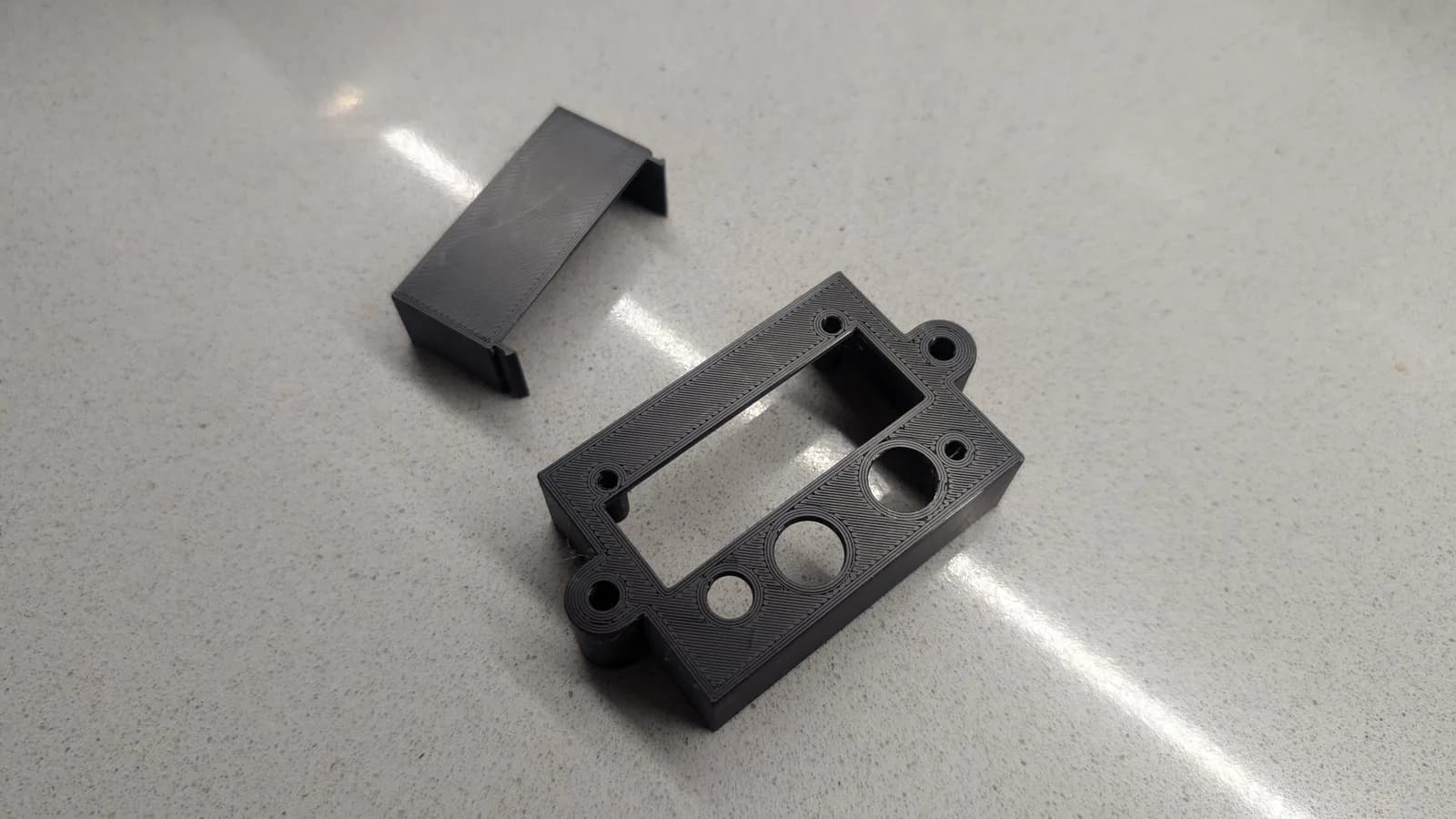 3D-printed black plastic shell components for PVM-14L1 RGB mod, showing rectangular cover and control panel with mounting holes and switch cutout.