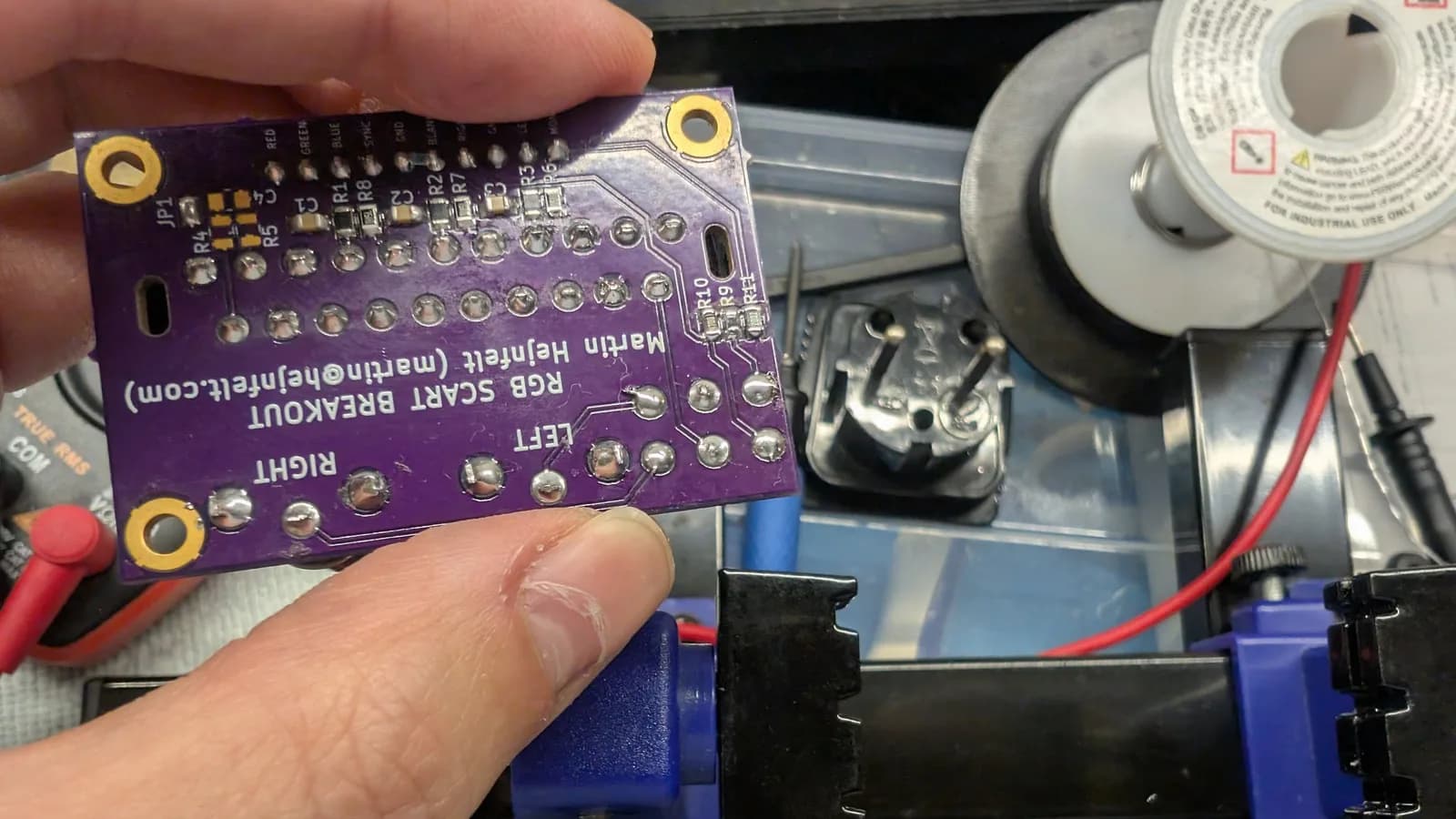 Purple RGB mod PCB held in hand, showing solder joints and component layout above CRT monitor chassis with wiring visible.