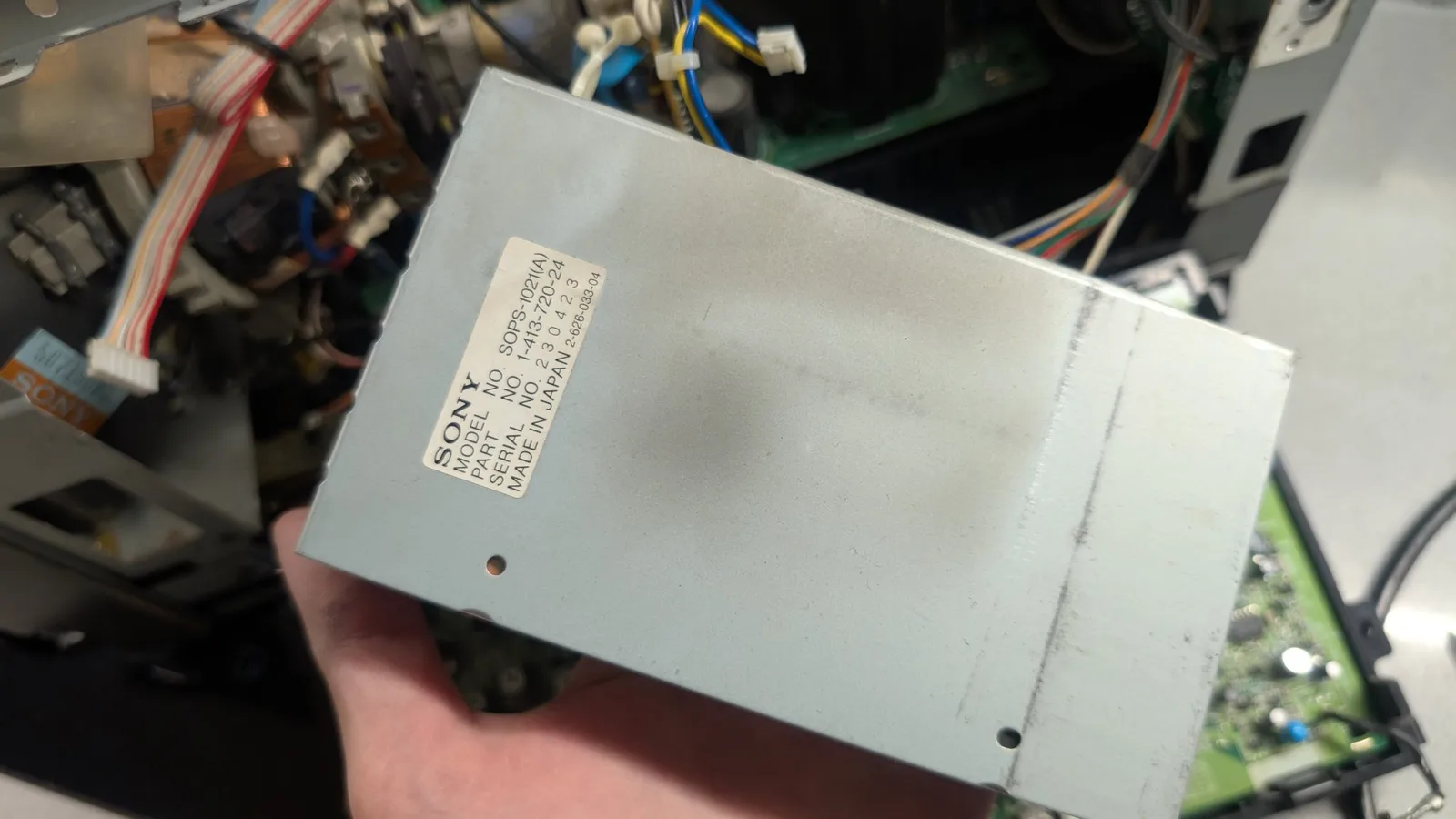 Sony PVM-6041Q power supply unit removed from chassis, showing label and mounting holes during capacitor replacement and solder reflow restoration.
