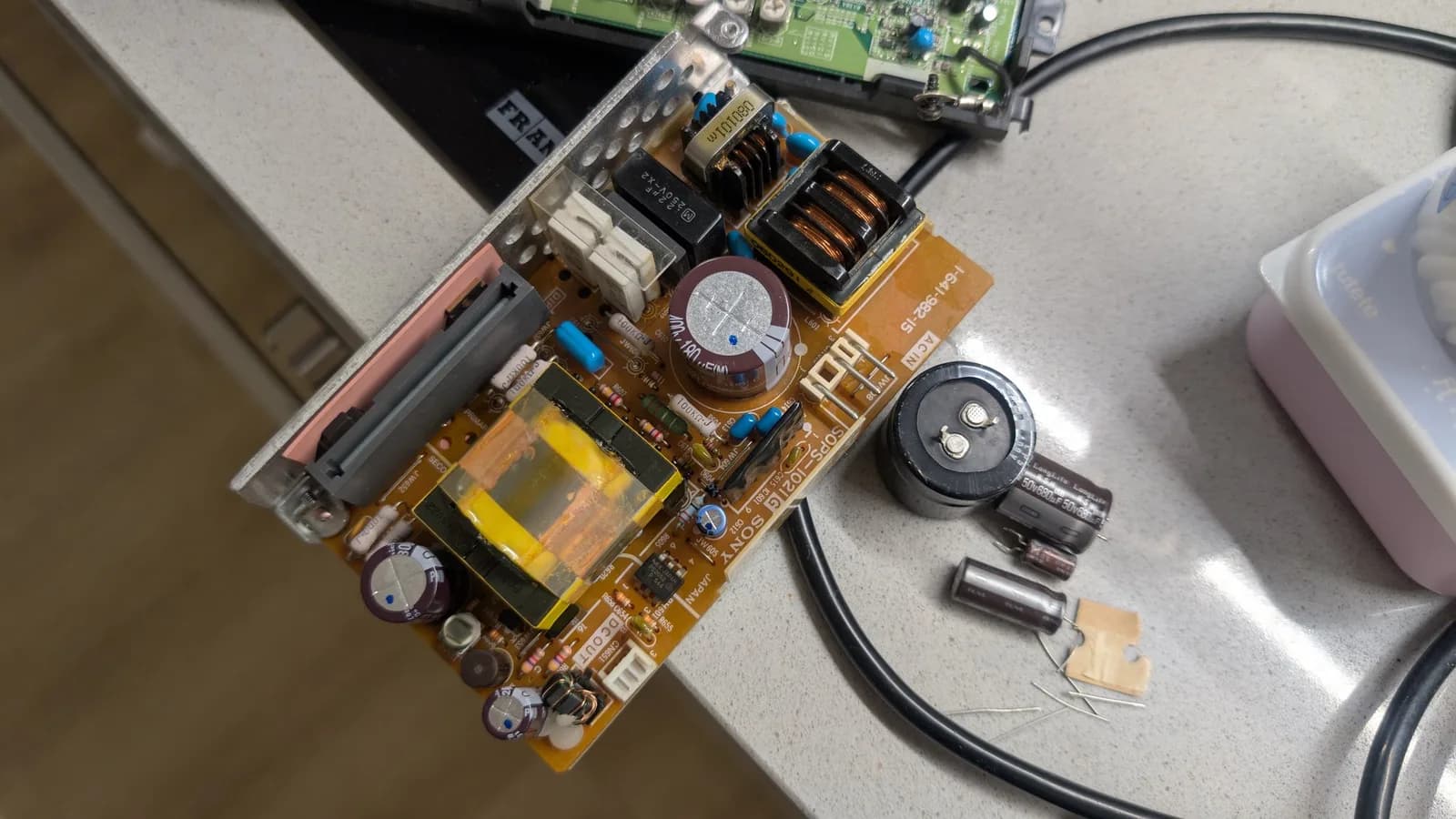 Disassembled Sony PVM-6041Q power supply board on workbench showing capacitors, transformers, and disconnected components during restoration.