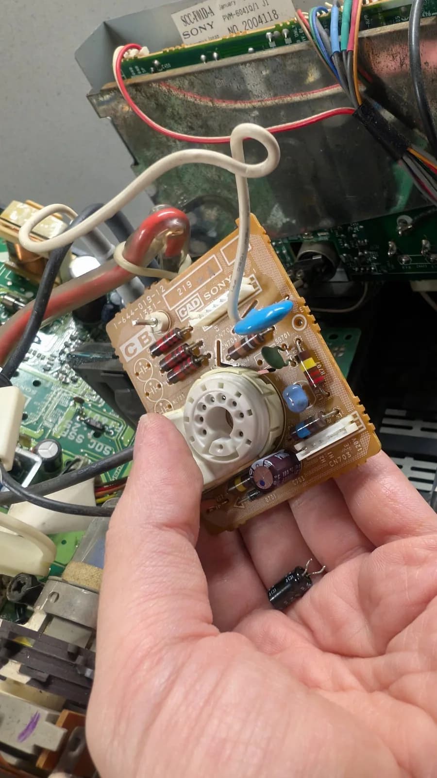 Technician's hand holding Sony neck board with dull solder joints visible on tube socket and components during reflow repair.