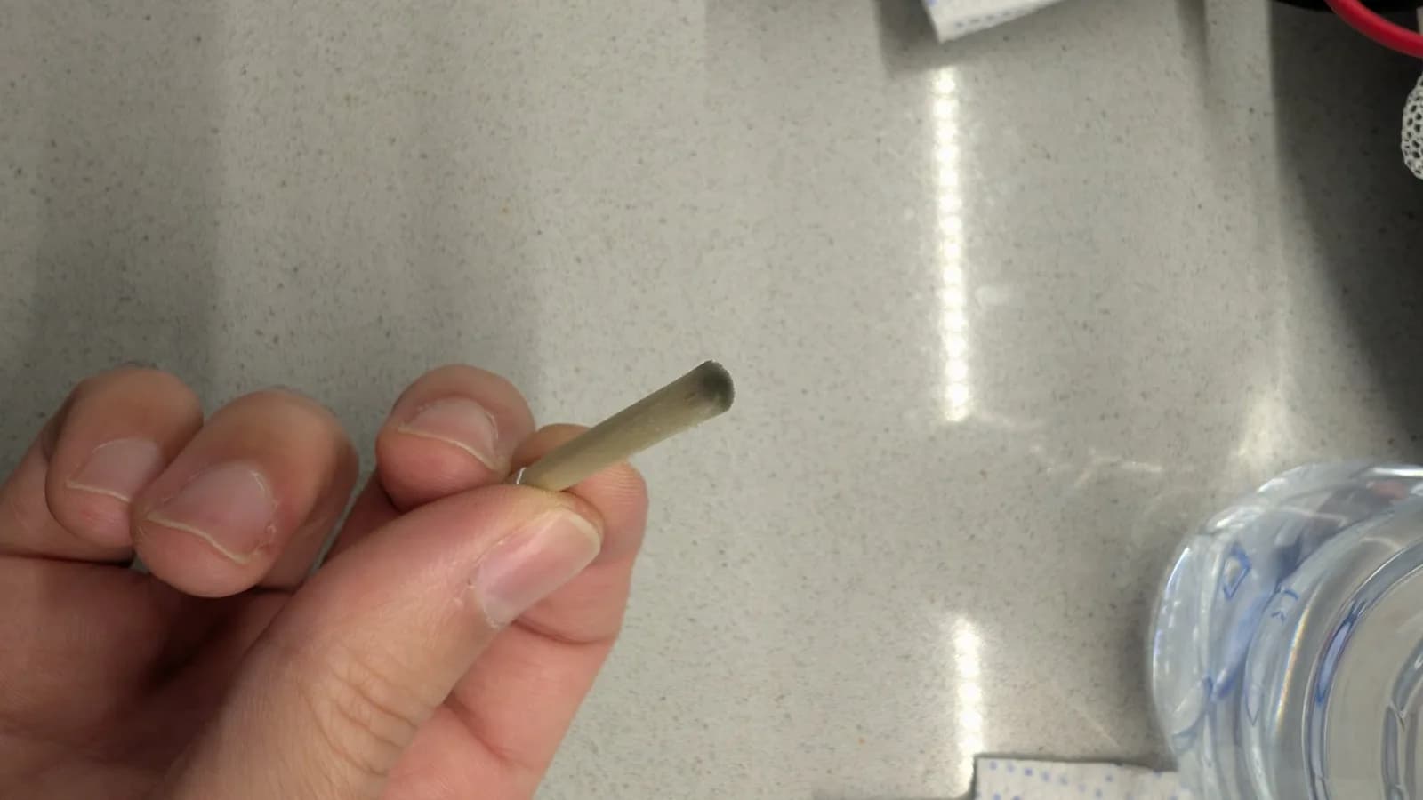 Hand holding fiberglass pen near CRT tube pins during oxidation cleaning with IPA and Deoxit on workbench.