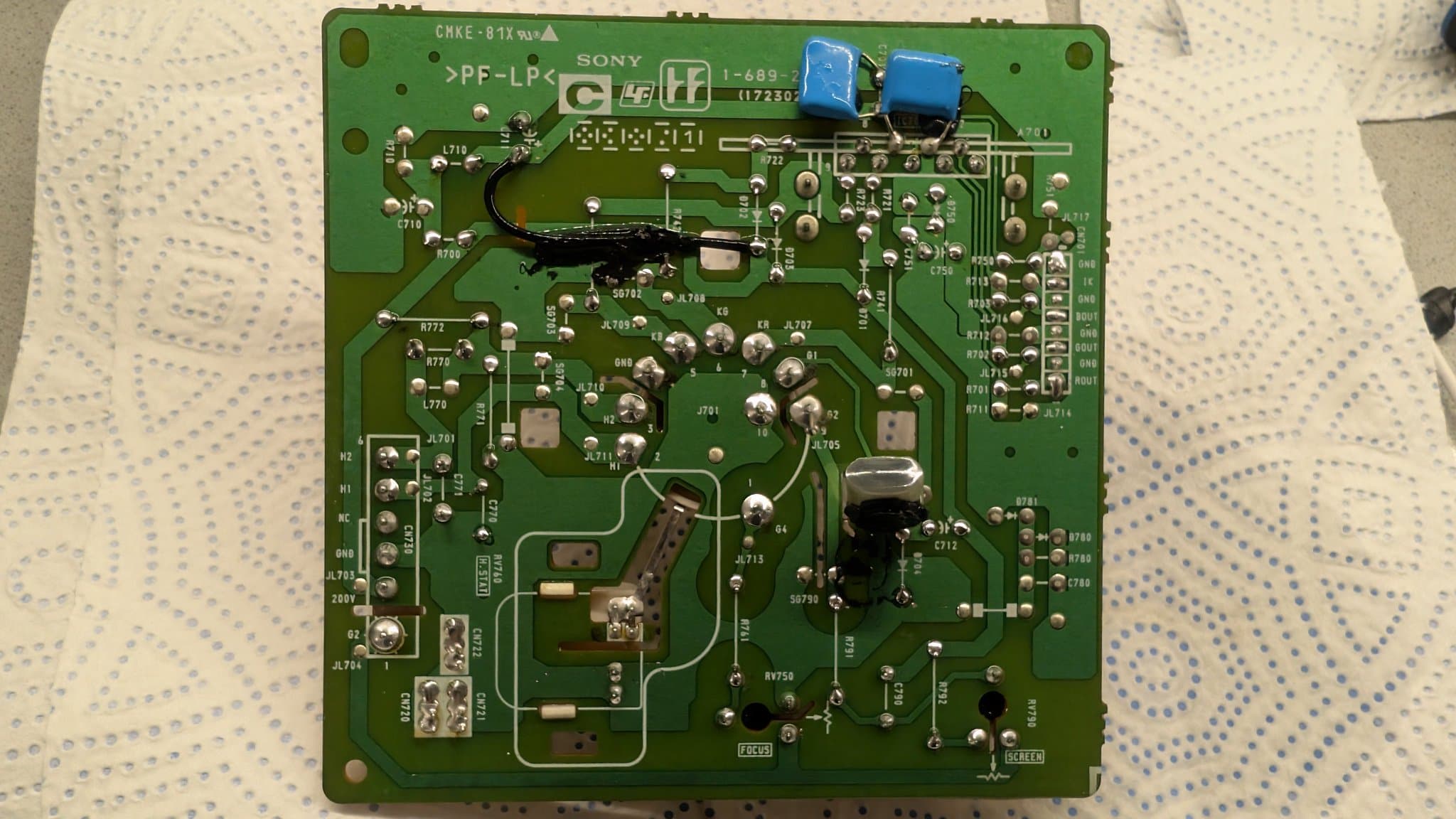Sony PVM-14L1 neck board with reflowed solder joints, blue capacitors visible at top, components and traces throughout green PCB.