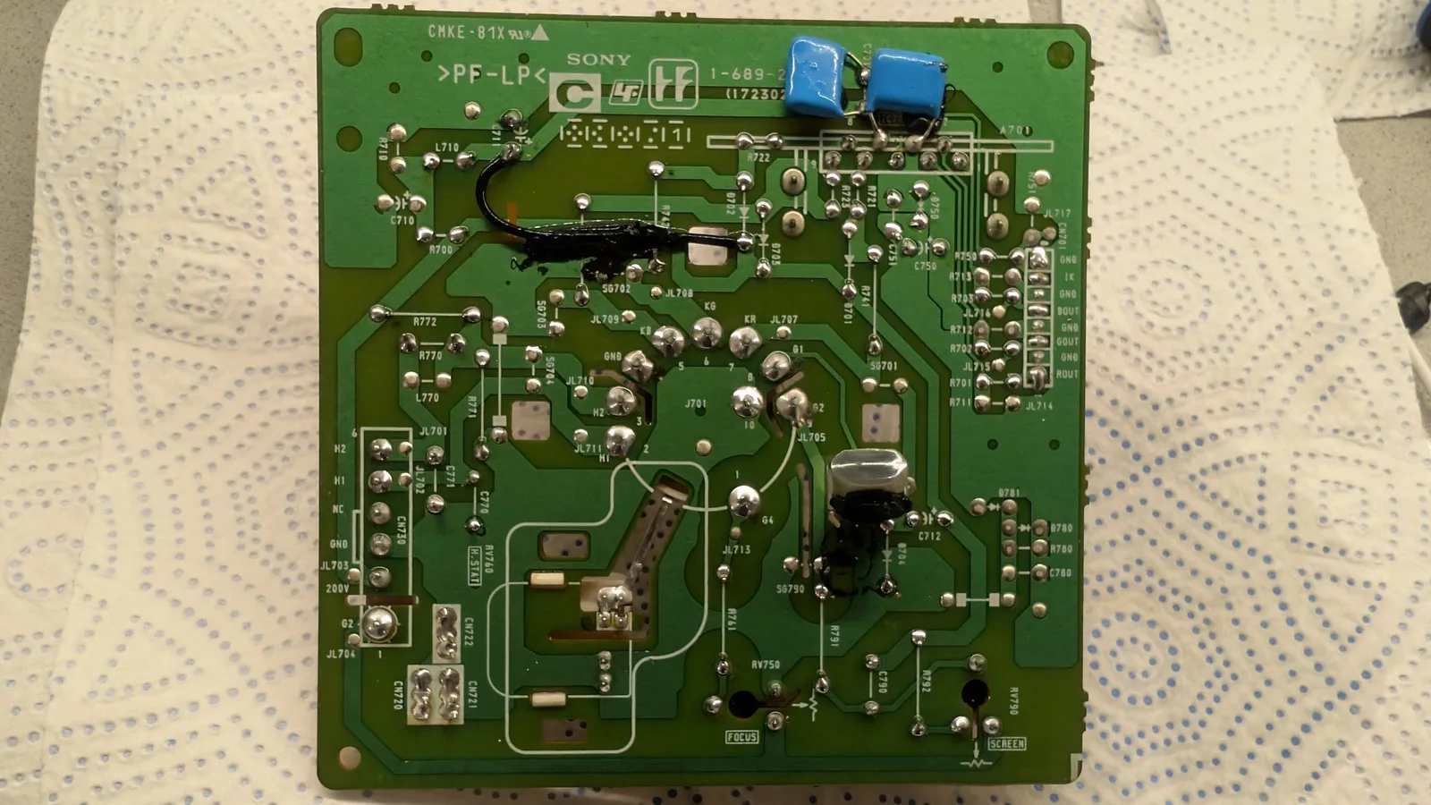 Sony PVM-14L1 neck board with reflowed solder joints, blue capacitors visible at top, components and traces throughout green PCB.