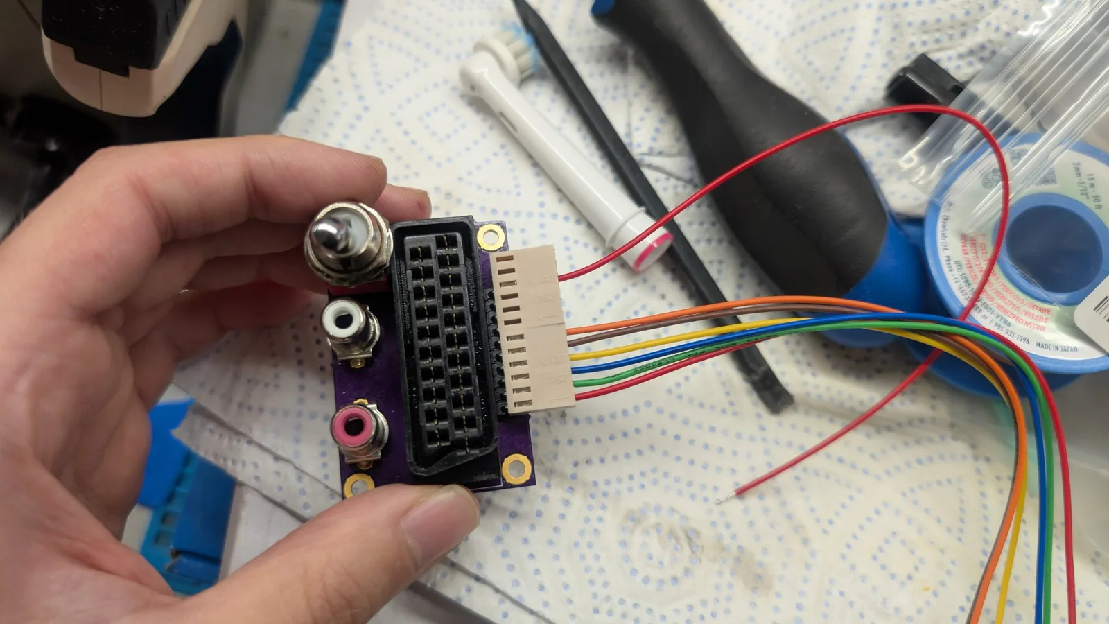 Custom SCART breakout board with soldered potentiometer, ribbon cable connector, and multicolored wire leads during RGB mod assembly.