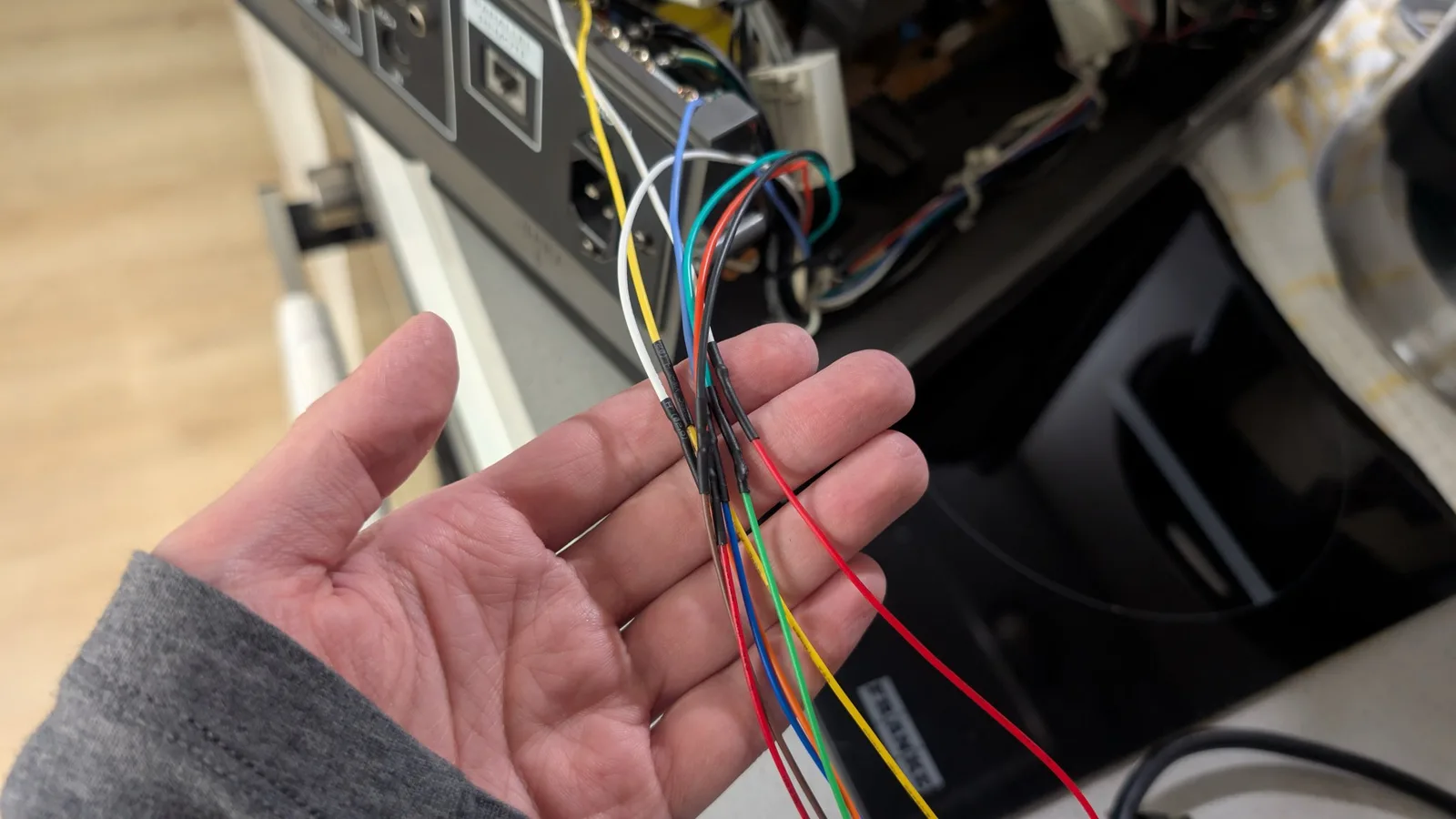Hand holding bundle of colored wires (red, blue, green, yellow, white, black) soldered to RGB mod connector during PVM-14L1 installation.
