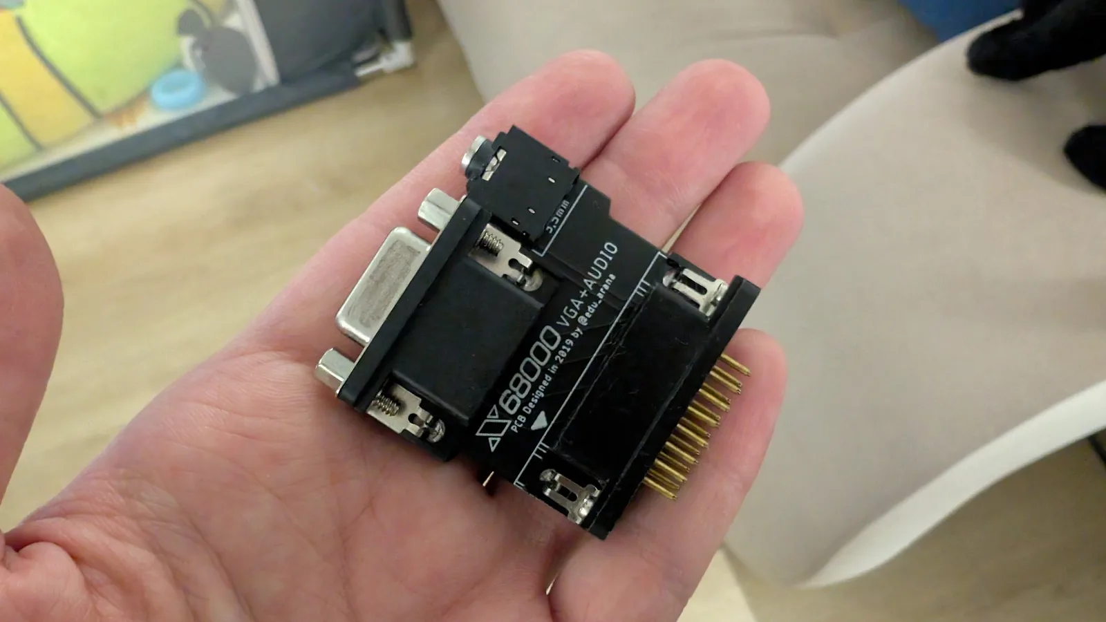 The edu_arana RGB-to-VGA adapter for the X68000 held in the palm, its D-sub connector and pin header visible, used to test the computer's output.