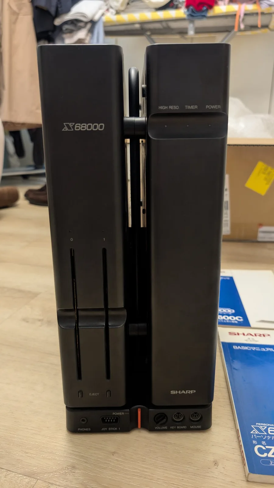The first-generation Sharp X68000 tower front-on, showing its X68000 branding, power button and front control panel, with some Japanese system manuals beside it.