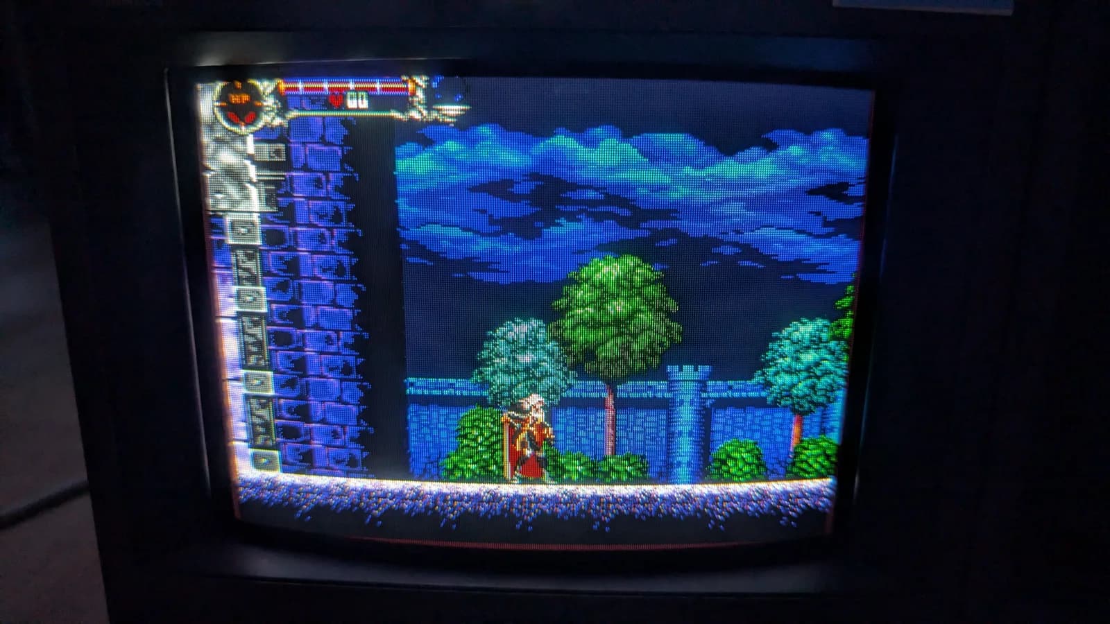Sony PVM-9041Q running the Mega Drive homebrew demake of Castlevania: Symphony of the Night after the deflection-board recap, Alucard before the castle wall under a blue sky with trees, the HP bar and item column at the left.