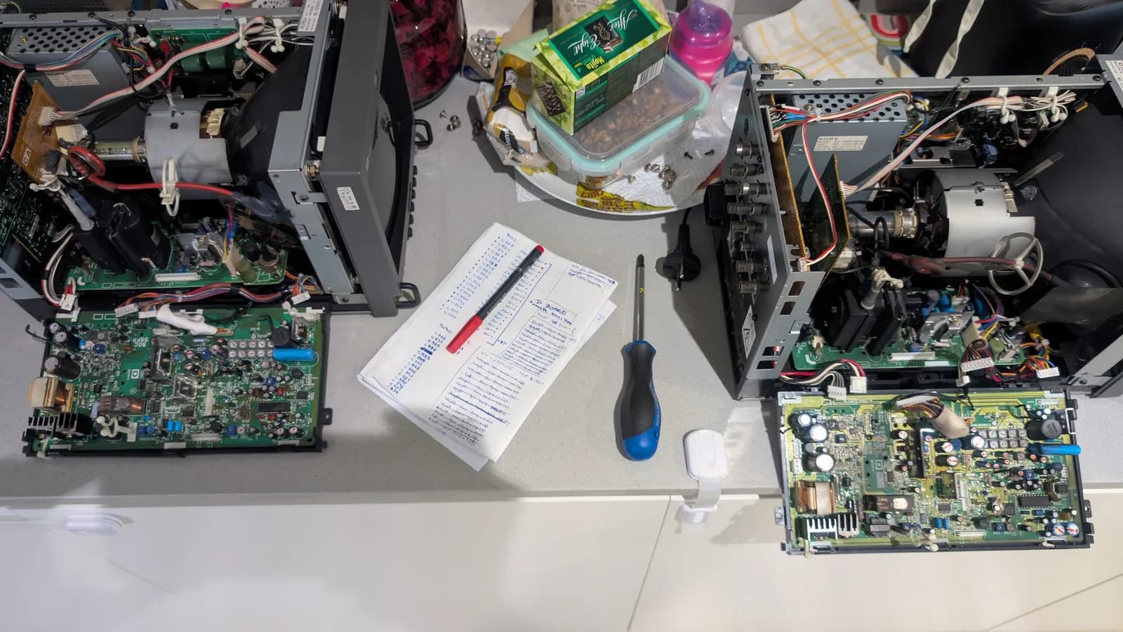 Two 9-inch Sony PVMs (the 9045QD and the 9041Q) opened side by side on the bench for deflection day, their boards out, with a handwritten list of the capacitors known to be most likely to fail and a screwdriver between them.
