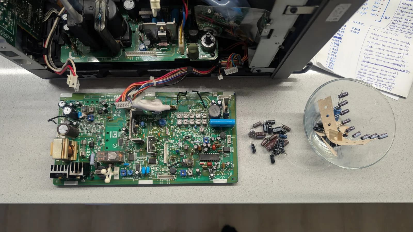 Sony PVM-9045QD deflection board not yet recapped, the old capacitors removed and set off to the side, the new capacitors displayed in a bowl ready to fit.