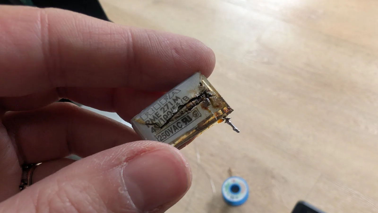 Burnt X2 safety capacitor held in fingers, showing catastrophic thermal damage and charring from the Beovision 1 repair.