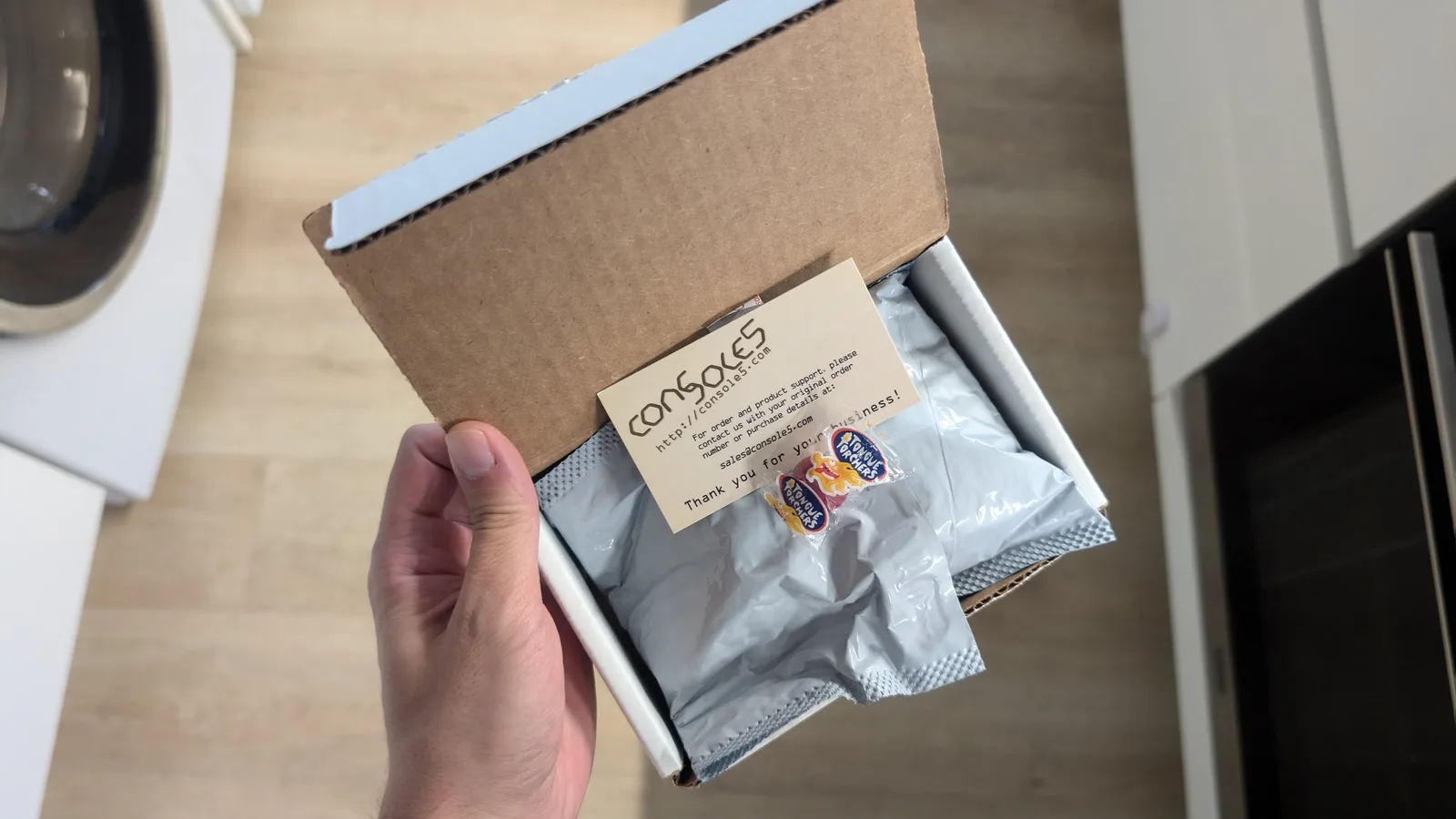 Hand holding open Console5 cardboard box containing silver drive belt package and thank you card for Sega Wondermega repair.