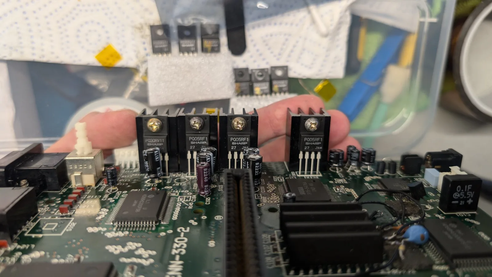 Close-up of four replacement voltage regulators (P005RF1) being held over a Sega Wondermega circuit board during repair work.